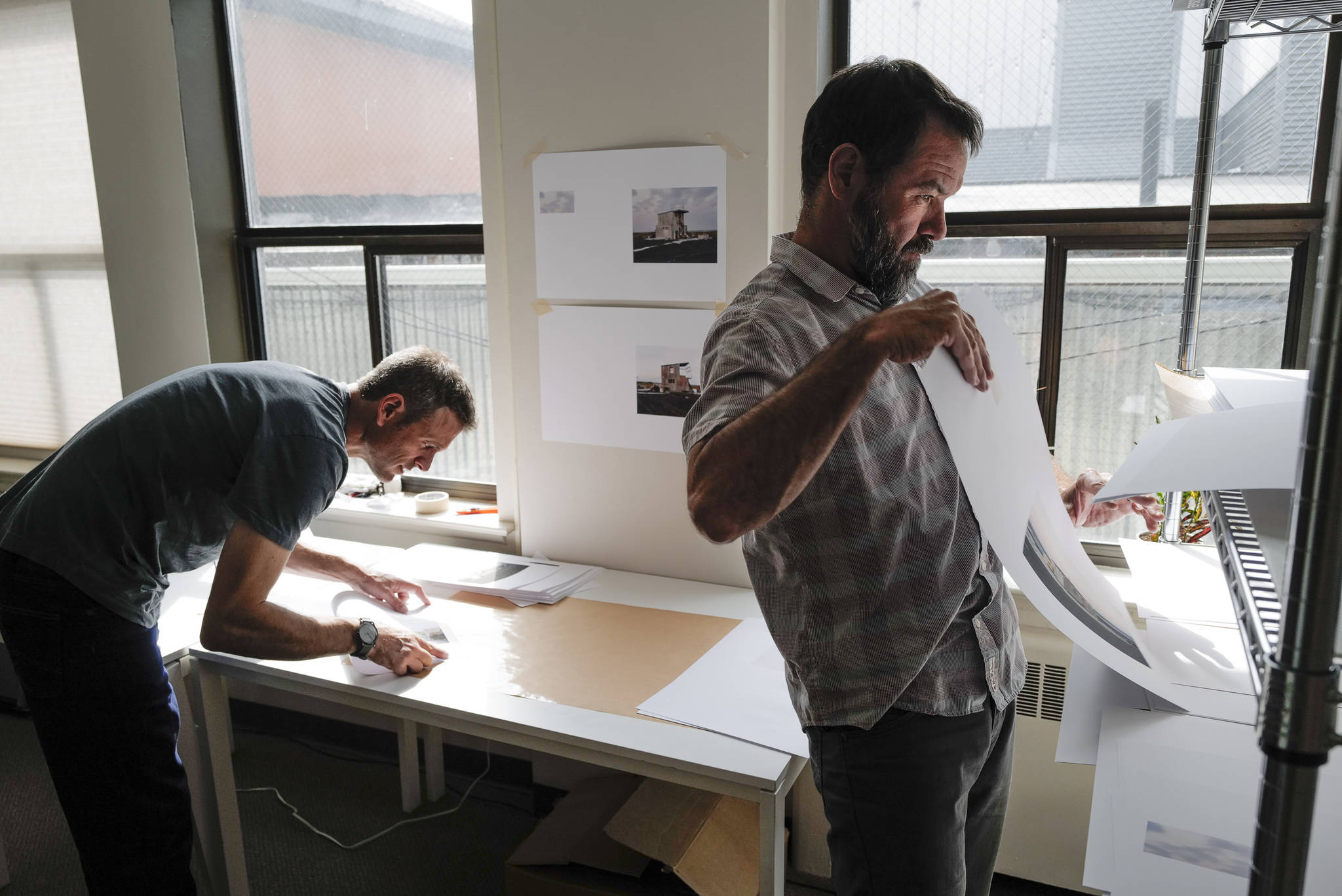 Seattle-based photographer Eirik Johnson, left, works with Ben Huff, a local photographer and editor of Ice Fog Press, on a hand-made book of Johnson’s photographs titled “Barrow Cabins” on Wednesday, Aug. 21, 2019. (Michael Penn | Juneau Empire)