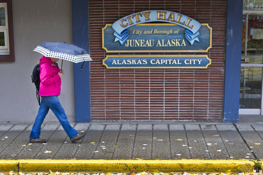 In this October 2015 file photo, maple leaves fall on Seward Street as a pedestrian ducks rain in front of City Hall. (Michael Penn | Juneau Empire File)