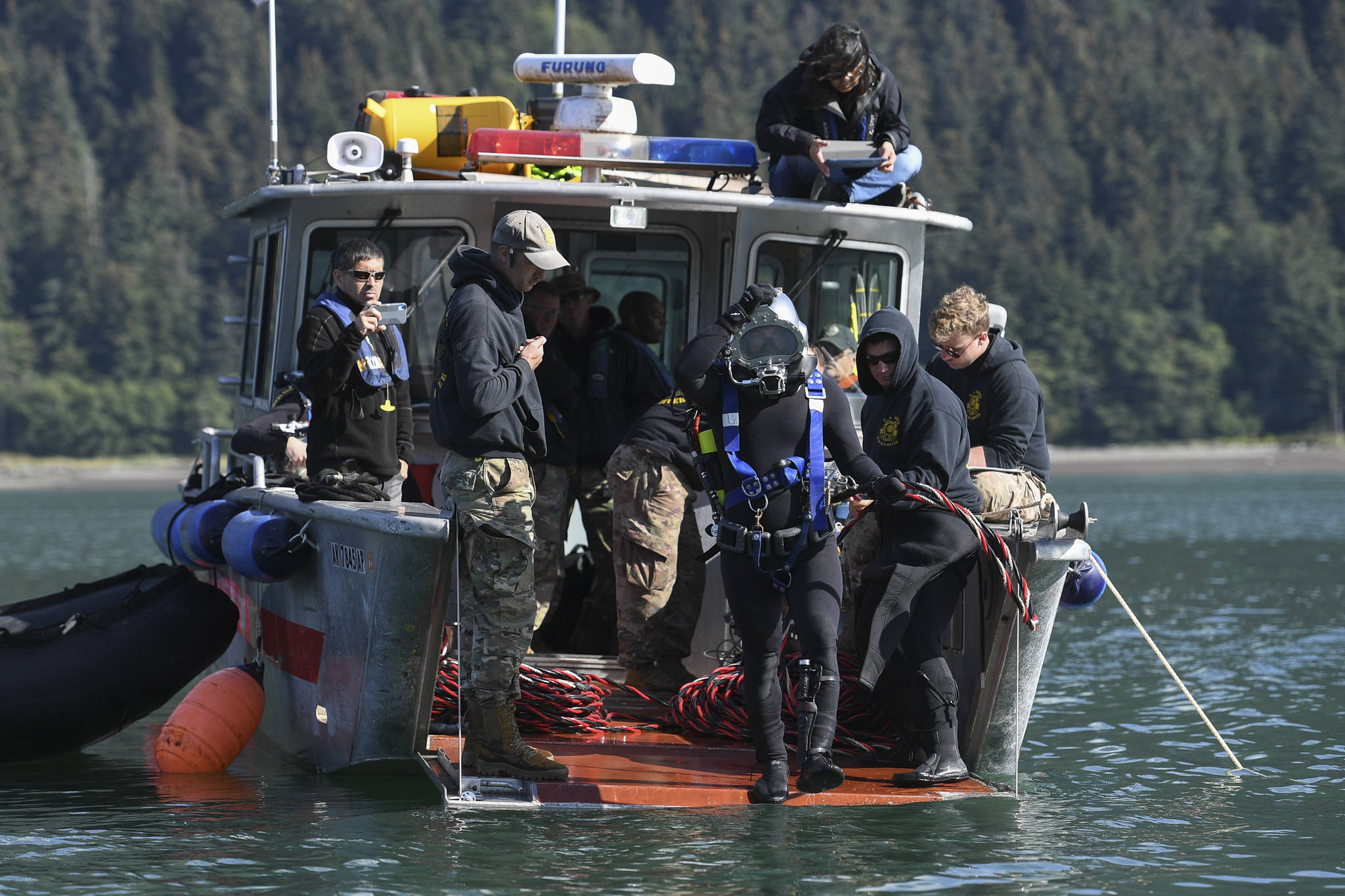 Spc. James Lewis, center, steps off the bow of a Juneau Harbormaster’s boat as members of the Army’s 74th Engineer Dive Detachment work to retrieve lost crab pots in Gastineau Channel for the Douglas Indian Association/NOAA Marine Debris Project on Thursday, Sept. 5, 2019. The project aims to identify and remove derelict crab pots and their continued negative impact on wildlife and the environment. (Michael Penn | Juneau Empire)