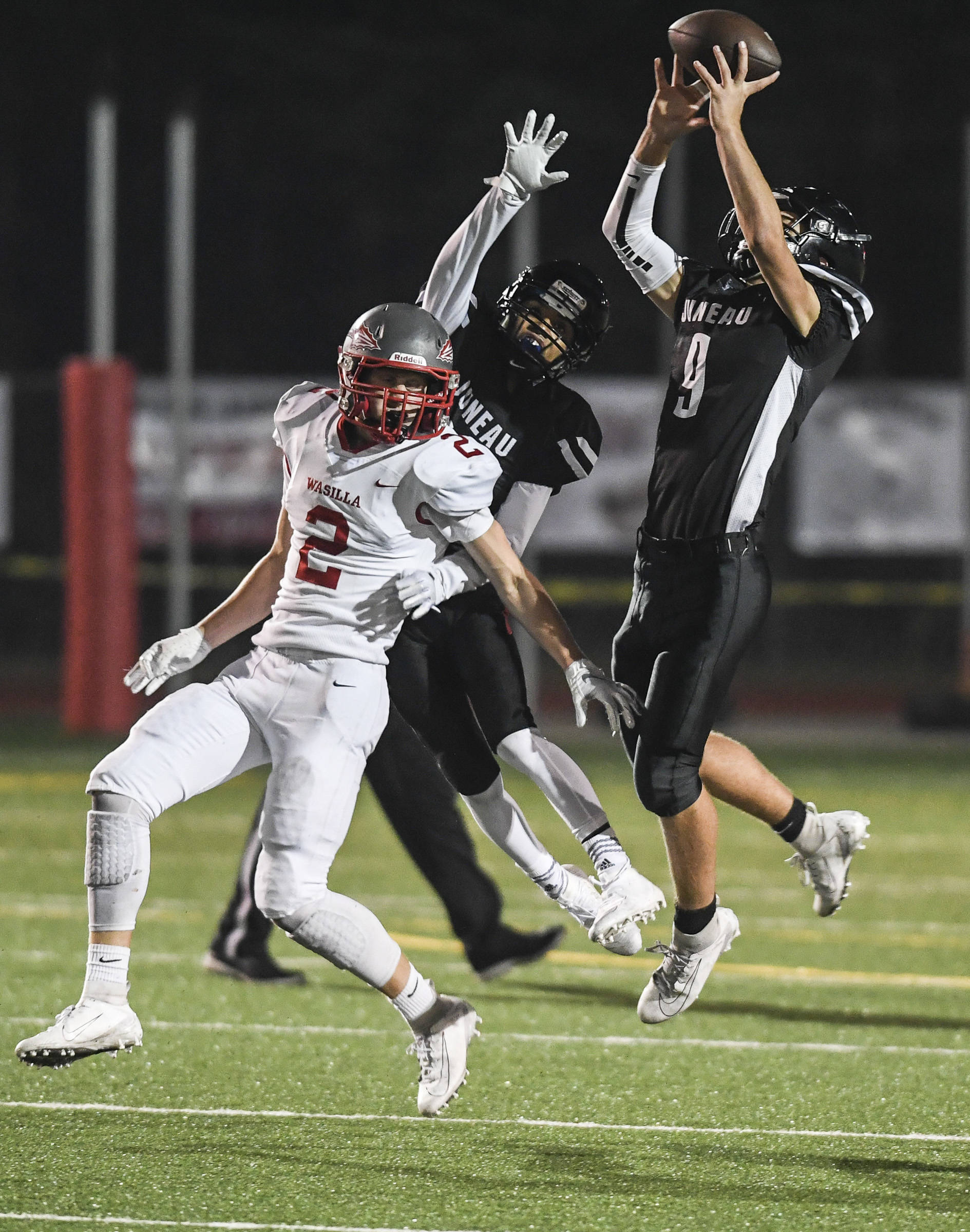 Juneau’s Wallace Adams, right, intercepts a pass intended for Wasilla’s Luke Devine, left, in the third quarter at Adair-Kennedy Memorial Field on Friday, Sept. 6, 2019. Juneau’s Jahrease Mays, center, was also in on the play. Juneau won 63-0. (Michael Penn | Juneau Empire)