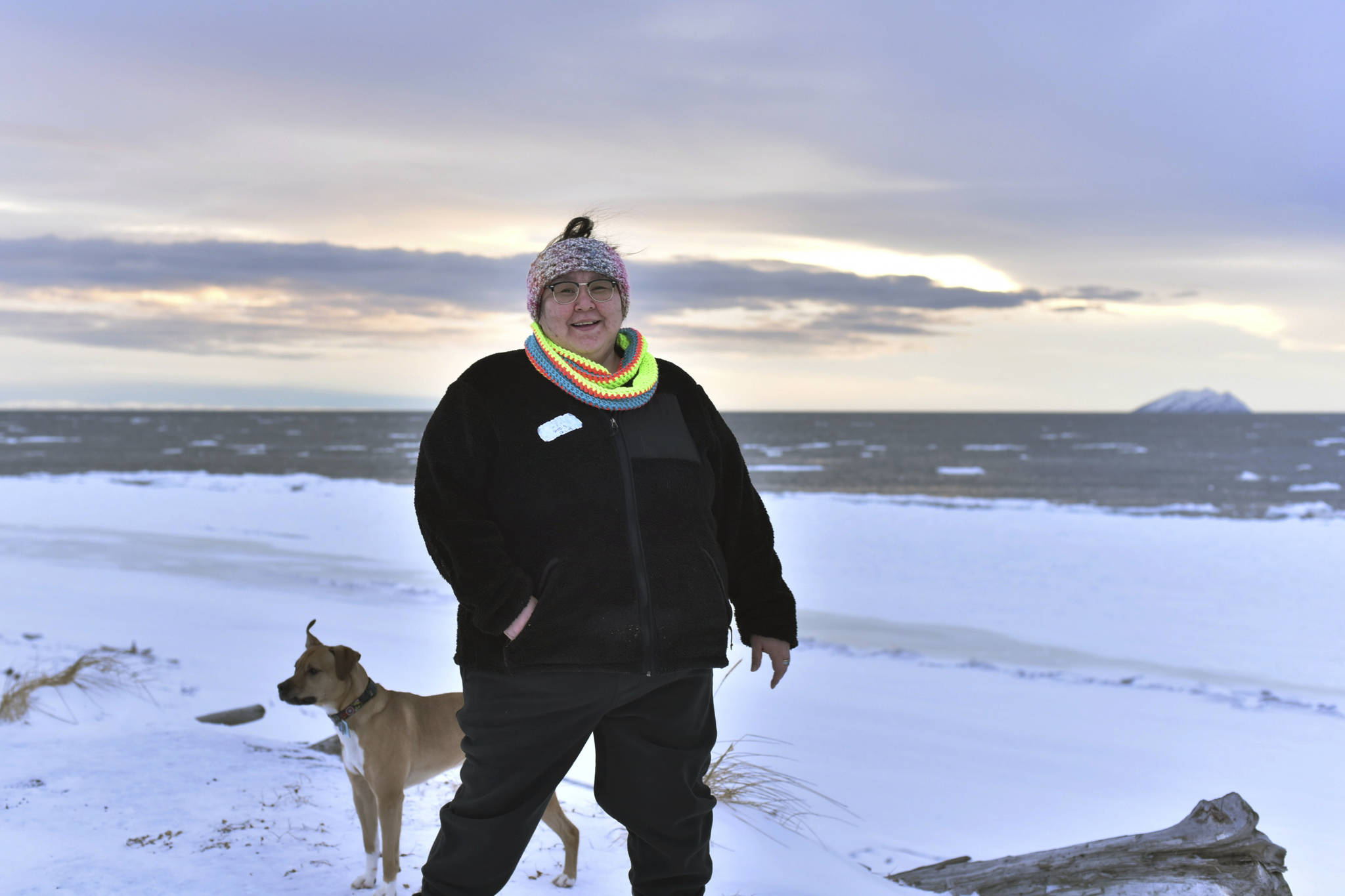 In this Jan. 14 photo, Clarice “Bun” Hardy stands on the beach with her dog, Marley, in the Native Village of Shaktoolik. Hardy, a former 911 dispatcher for the Nome Police Department, says she moved back to her village after a sexual assault left her feeling unsafe in Nome. (AP Photo | Victoria Mckenzie)