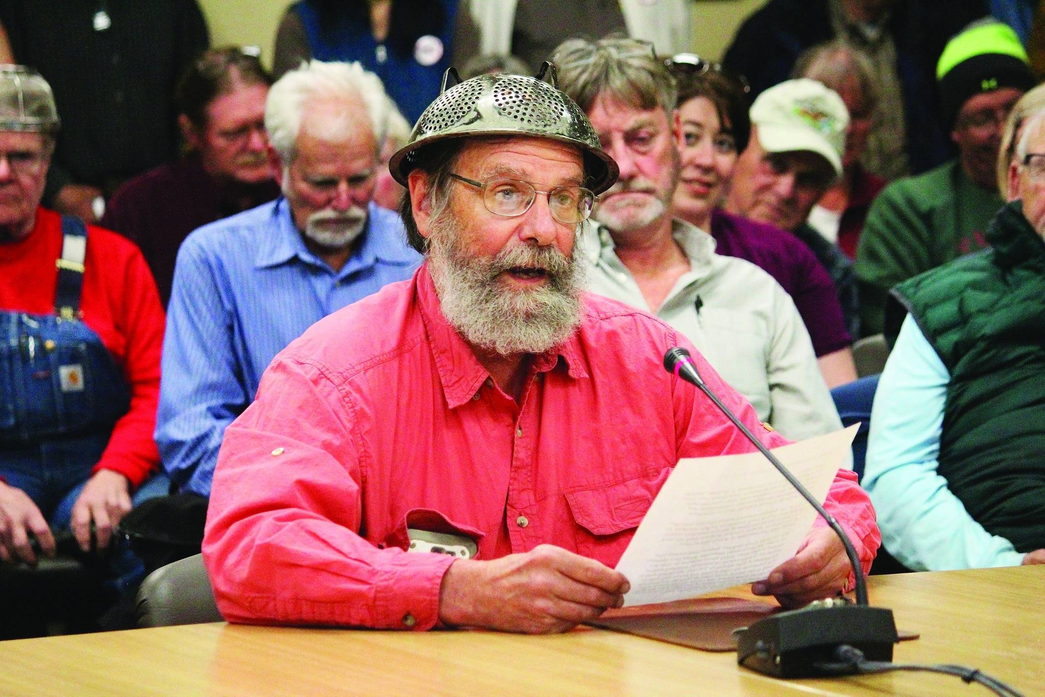 Fritz Creek area resident Barrett Fletcher gives the invocation before a Kenai Peninsula Borough Assembly meeting as a representative of the Church of the Flying Spaghetti Monster at Homer City Hall in Homer, Alaska, Tuesday, Sept. 18, 2019. A pastor wearing a spaghetti strainer on his head delivered the opening invocation at the Kenai Peninsula Borough Assembly meeting Tuesday. The invocation by the pastor of the Homer congregation of the Church of the Flying Spaghetti Monster is the second non-traditional invocation before the assembly since a court ruling. (Megan Pacer/Homer News via AP)