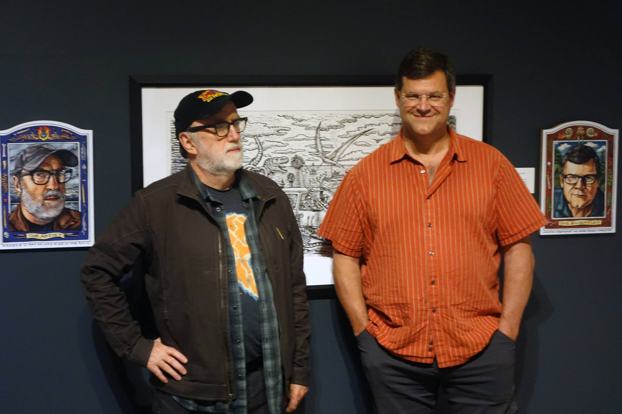Ketchikan artist Ray Troll and Smithsonian National Museum of Natural History Director Kirk Johnson stand together in the Alaska State Museum near their Troll-drawn portraits. “Cruising’ the Fossil Coastline” is a traveling exhibition inspired by Troll and Johnson’s collaborative book. Johnson was in town Tuesday to talk at the museum. (Ben Hohenstatt | Capital City Weekly)