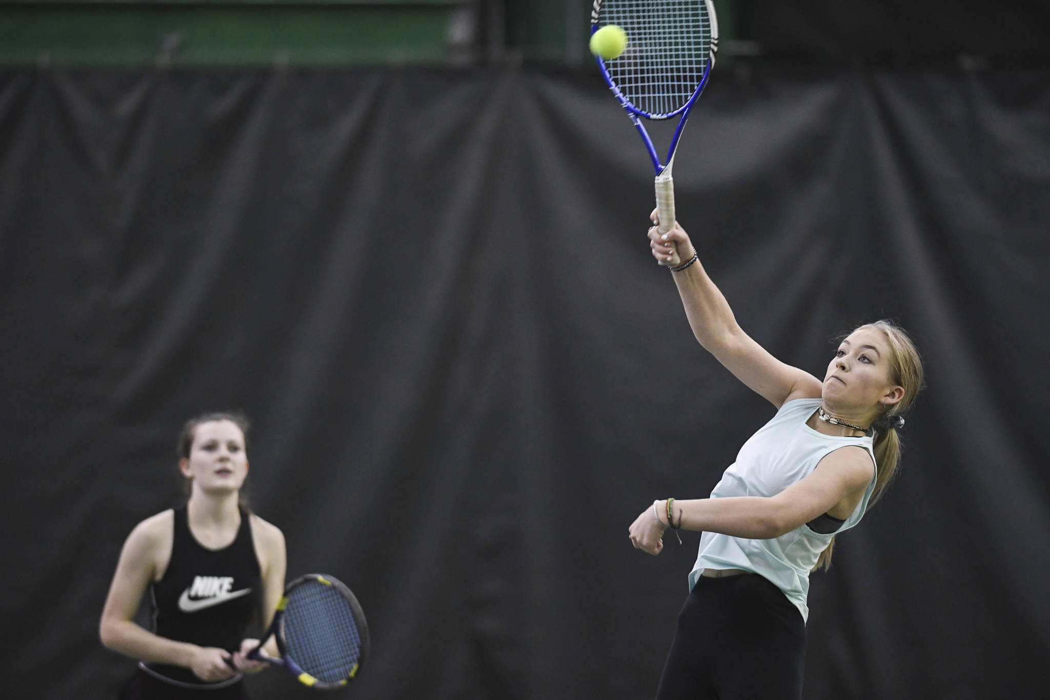 Jaymie Collman hits an overhead as she plays in the girls doubles’ final with partner Katie Pikul, background, against Adelie McMillan and Olivia Moore during the Region V Tennis Tournament at The Alaska Club/JRC on Saturday, Sept. 28, 2019. McMillan/Moore won 7-6, 6-4. (Michael Penn | Juneau Empire)