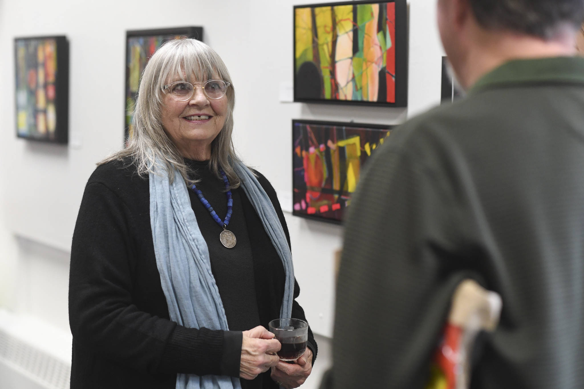 Mary Ida Henrikson talks with viewers of her oil paintings “Beyond the Pale,” on display at the Juneau Arts & Culture Center during First Friday on Oct. 4, 2019. (Michael Penn | Juneau Empire)