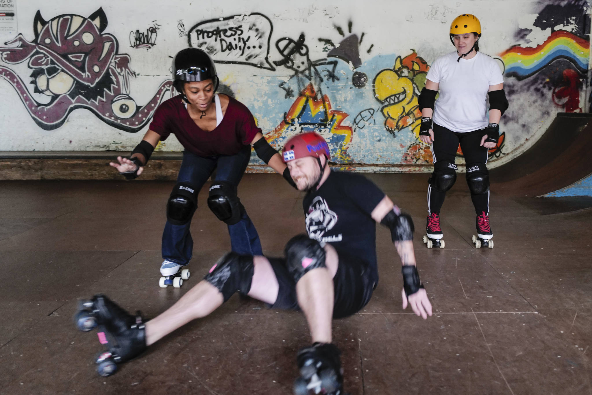 Empire reporter Michael S. Lockett takes a fall while being taught to rollerskate by Jennifer Gross, left, and Shabadrang Khalsa, at the Pipeline Skate Park on Friday, Oct. 11, 2019. (Michael Penn | Juneau Empire)