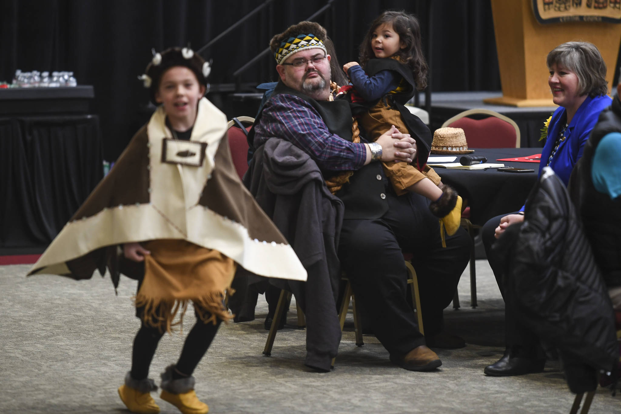 Richard Chalyee Éesh Peterson, President of the Central Council of Tlingit and Haida Indian Tribes of Alaska, holds Guillermo Contreras, 3, as Tristen Washington, 9, of the Xaadaas Dagwii Dance Group performs at the Elizabeth Peratrovich Hall for Indigenous Peoples’ Day on Monday, Oct. 14, 2019. (Michael Penn | Juneau Empire)