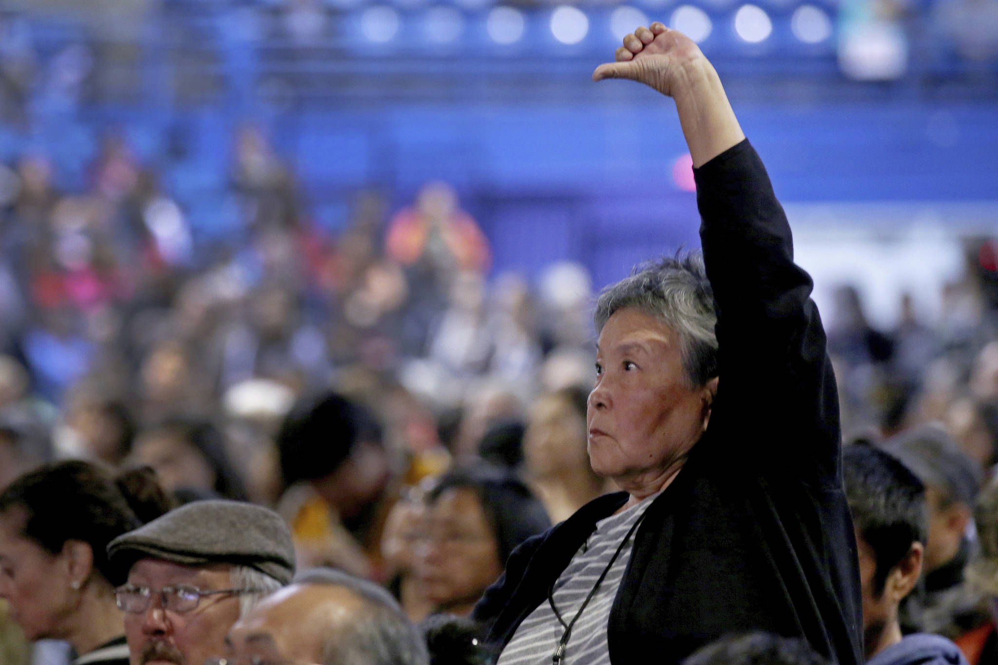 Dorothy Thomson stands while giving a thumbs down as Gov. Mike Dunleavy gives his State of Alaska Address during the 2019 Alaska Federation of Natives Convention Thursday, Oct. 17, 2019, in Fairbanks, Alaska. Republican Alaska Gov. Mike Dunleavy outlined plans aimed at improving public safety in rural Alaska during a speech Thursday to a major gathering of Alaska Natives that was interrupted by protests.(Eric Engman/Fairbanks Daily News-Miner via AP)