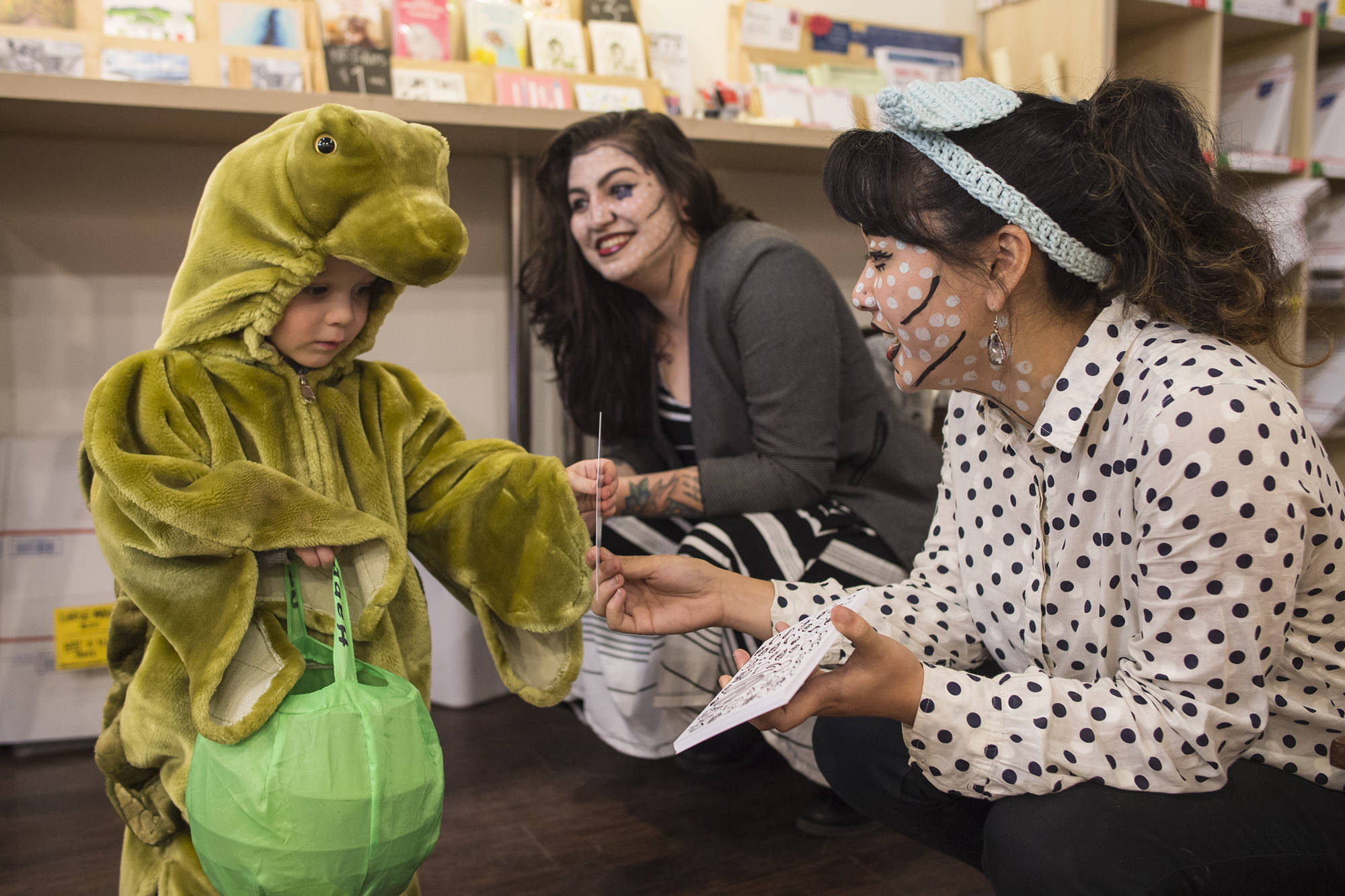 Corbin Hall, 2, receives a postcard from Rebecca Hsieh, right, and Kristen Cornell at Kindred Post for Halloween 2018. (Michael Penn | Juneau Empire)