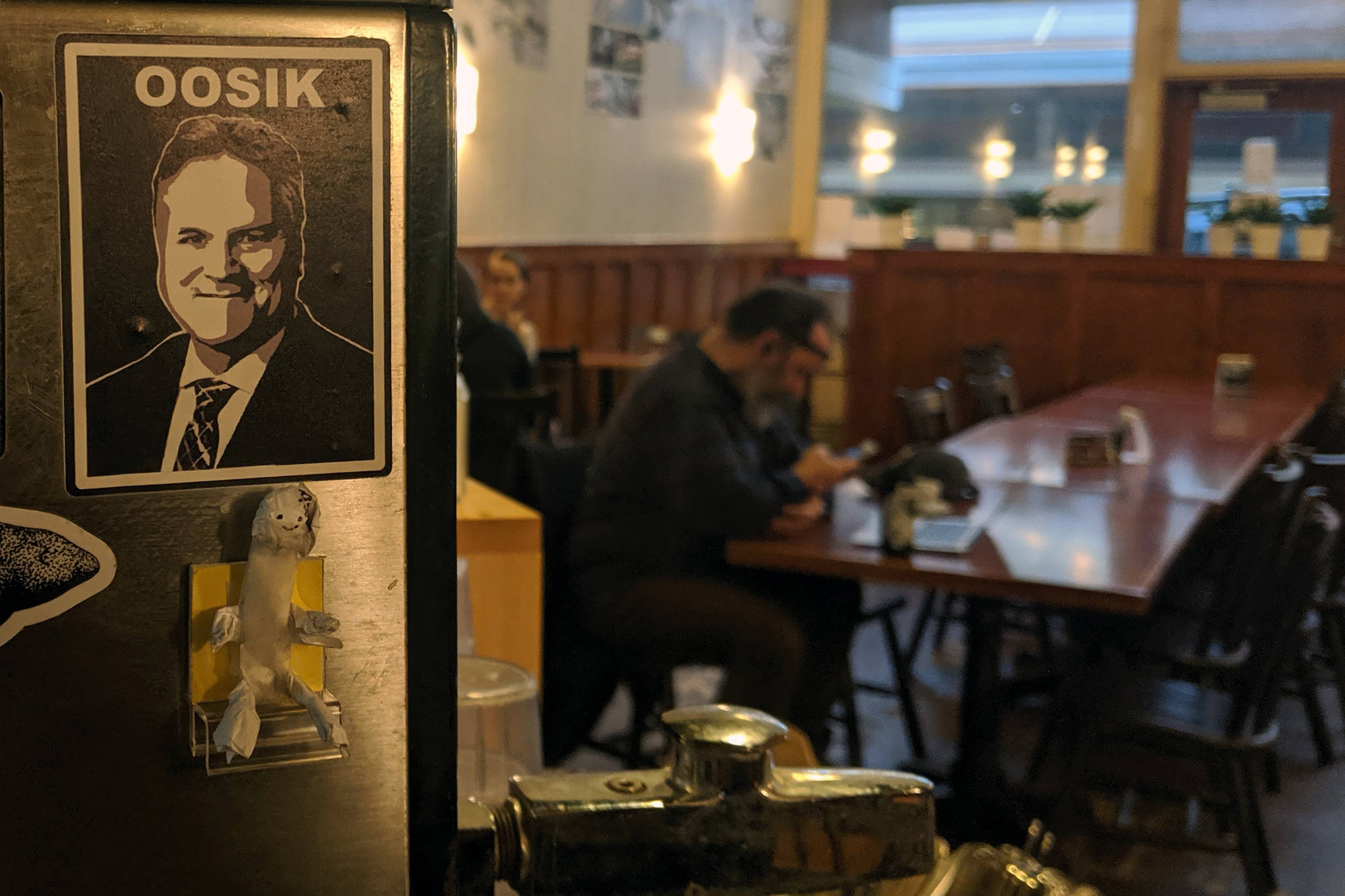 A sticker featuring Gov. Mike Dunleavy and the uniquely Alaskan insult, “Oosik,” can be seen in the Rookery Cafe. The artist behind the sticker Matt Hamilton said he bears Dunleavy no ill will. (Ben Hohenstatt | Capital City Weekly)