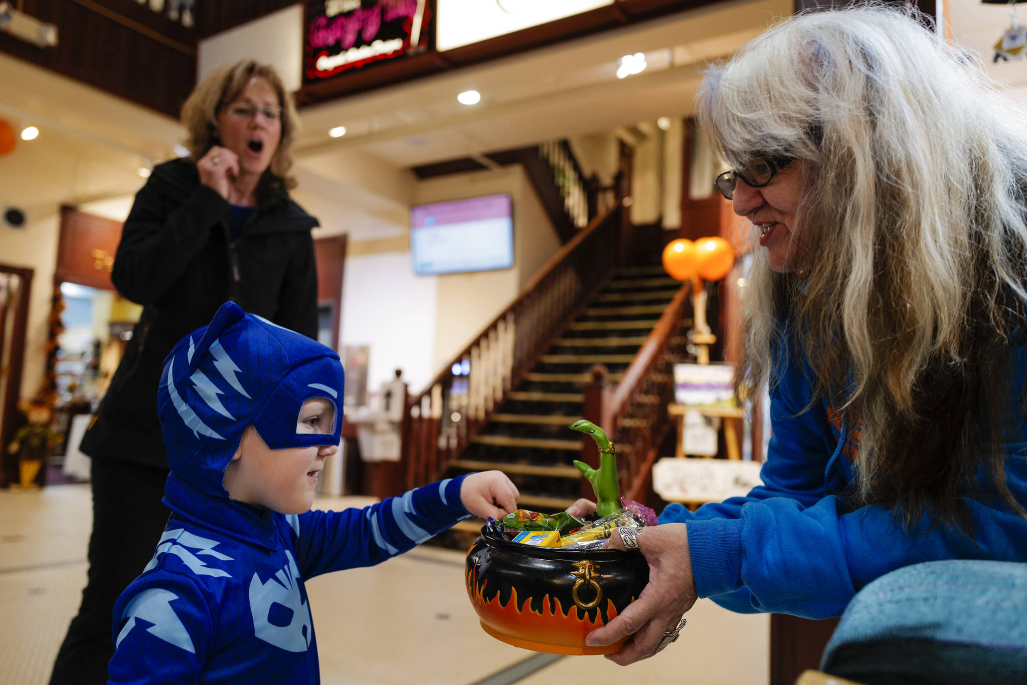 Dorain Gross, left, reacts as her grandson, Thorin Lombard, 3, reaches for a candy dish offered by Michelle of The Bear’s Lair during the Trick or Treat Downtown event on Thursday, Oct. 31, 2019. More than 70 business put out orange balloons to participate in the event aimed at young children. (Michael Penn | Juneau Empire)