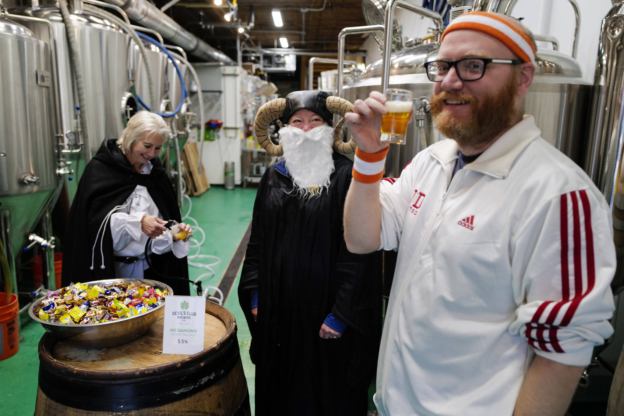 Aaron Suring takes advantage of the adult treat offered by Rachel Sanders, center, and TJ Thomson at the Devil’s Club Brewing Company during the Trick or Treat Downtown event on Thursday, Oct. 31, 2019. More than 70 business put out orange balloons to participate in the event aimed at young children. (Michael Penn | Juneau Empire)
