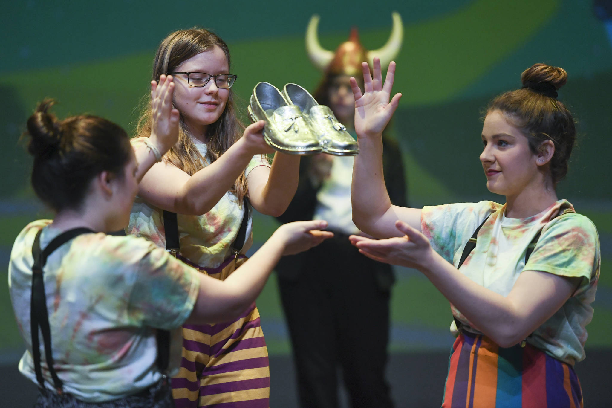 Munchkins Elena Lohrey, Caitlin Parker and River Carroll display the dead witch’s shoes during rehearsal for the Thunder Mountain High School production of “Choose Your Own Oz” at TMHS on Friday, Nov. 8, 2019. (Michael Penn | Juneau Empire)