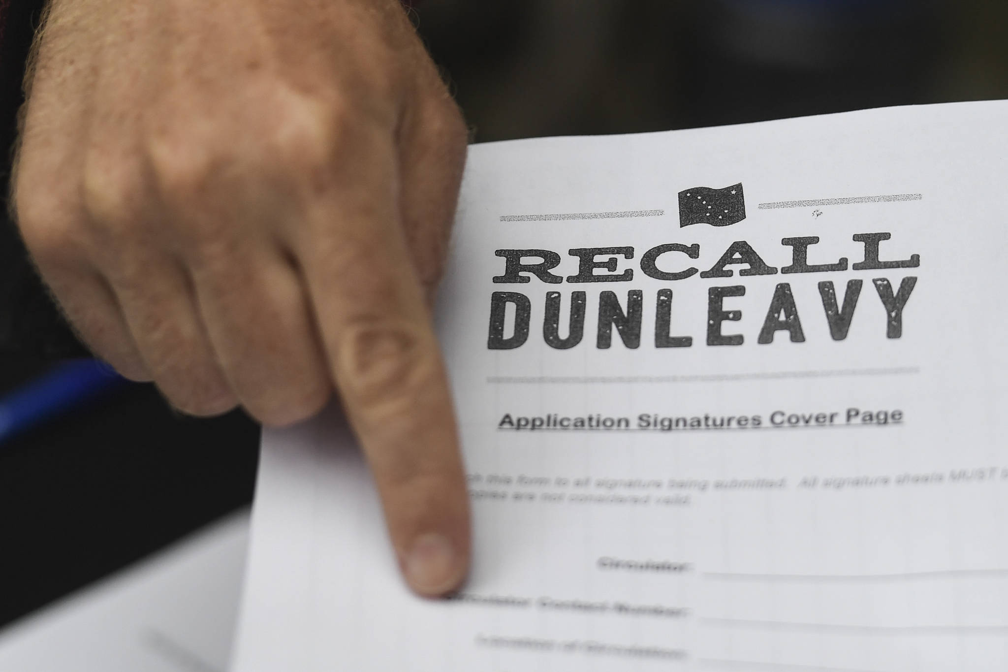 A Juneau resident holds up an application petition to recall Gov. Mike Dunleavy outside of the Planet Alaska Gallery on Thursday, Aug. 1, 2019. (Michael Penn | Juneau Empire File)