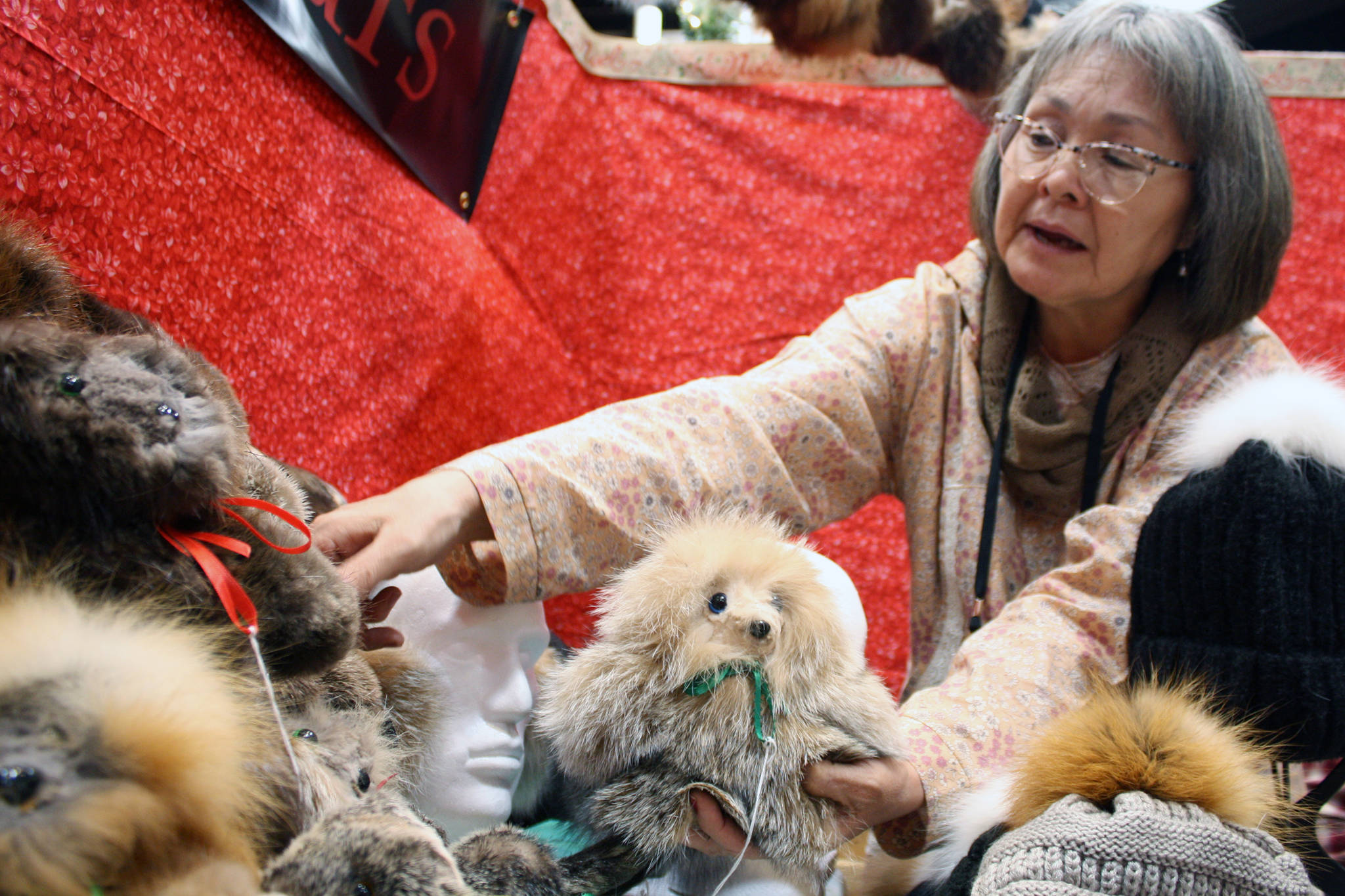Annie Fritze of Dillingham moves stuffed animals made of fur at Juneau Public Market, Friday Nov. 30, 2019. The handmade creatures were created using a variety of furs, including otter and lynx. (Ben Hohenstatt | Juneau Empire)