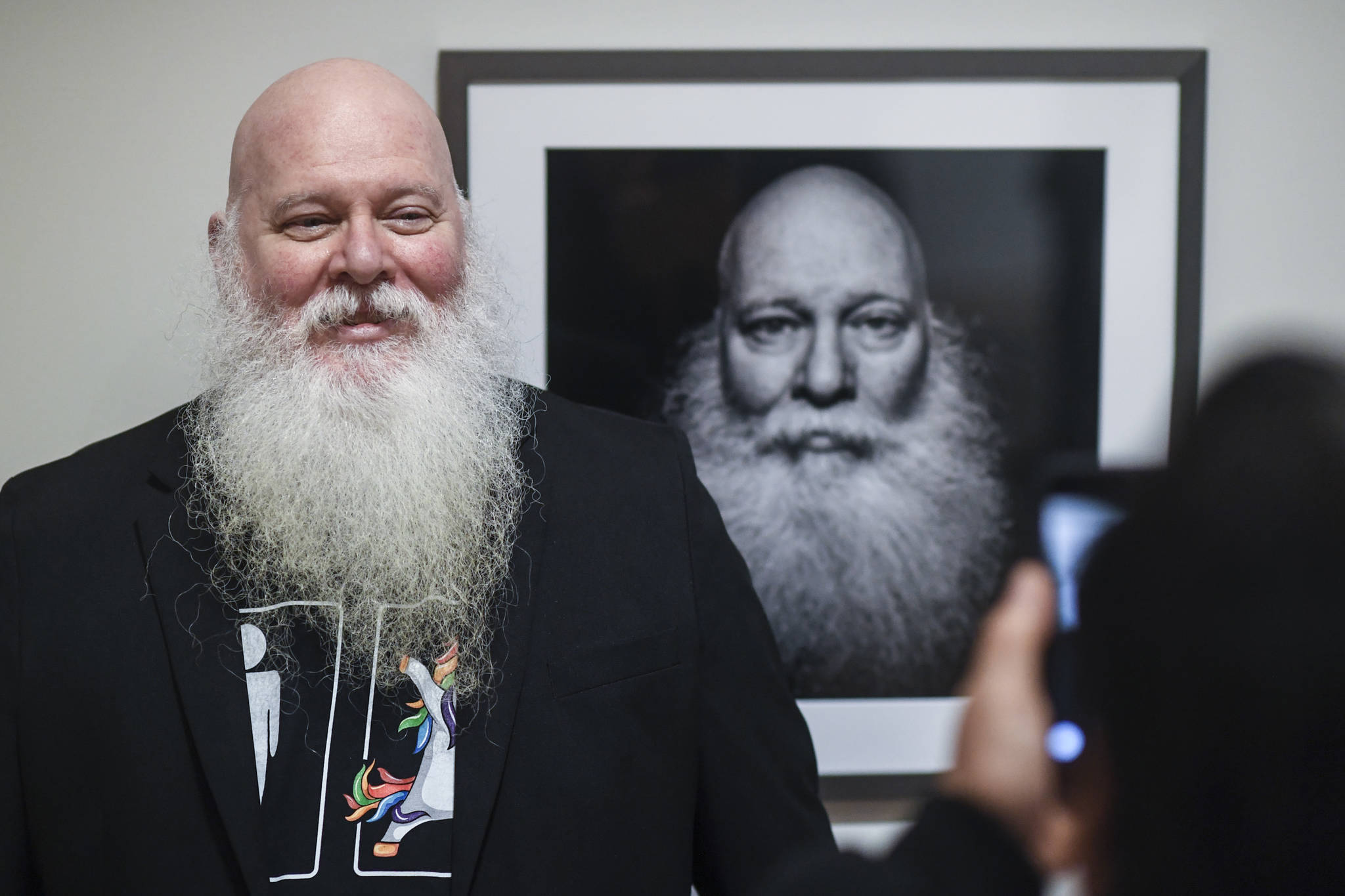 Mike Gates of Ketchikan has his picture taken by friend Dan Dawson in front of his self portrait at the Alaska Positive juried photography exhibit at the Alaska State Museum during Gallery Walk on Friday, Dec. 6, 2019. Gates received an Award of Recognition for his self portrait. (Michael Penn | Juneau Empire)
