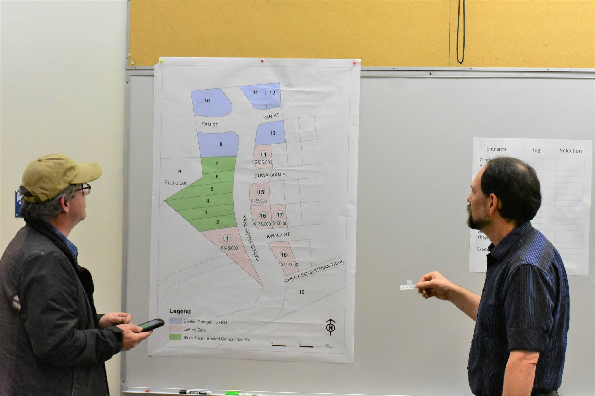 Rich Petersen of Lowpete Construction, left, gets first pick of available lots in the Pederson Hill subdivision while Land Manager Greg Chaney, right, awaits his decision at Juneau City Hall on Tuesday, Dec. 10, 2019. (Peter Segall | Juneau Empire)