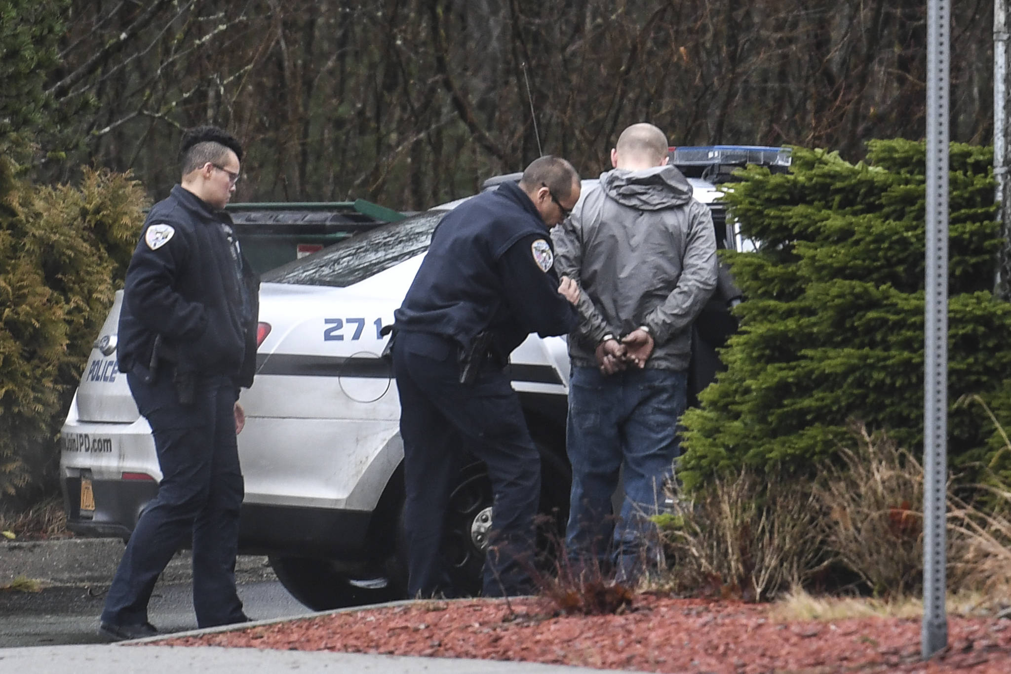 Juneau Police Officer Jim Quinto, center, and CJ Warnaca put Nick Morgan into the back of a police cruiser at the Department of Transportation and Public Facilities Buildig on Channel Drive on Wednesday, Dec. 11, 2019. Morgan was a suspect involved with a stolen vehicle parked in the department’s lot. (Michael Penn | Juneau Empire)