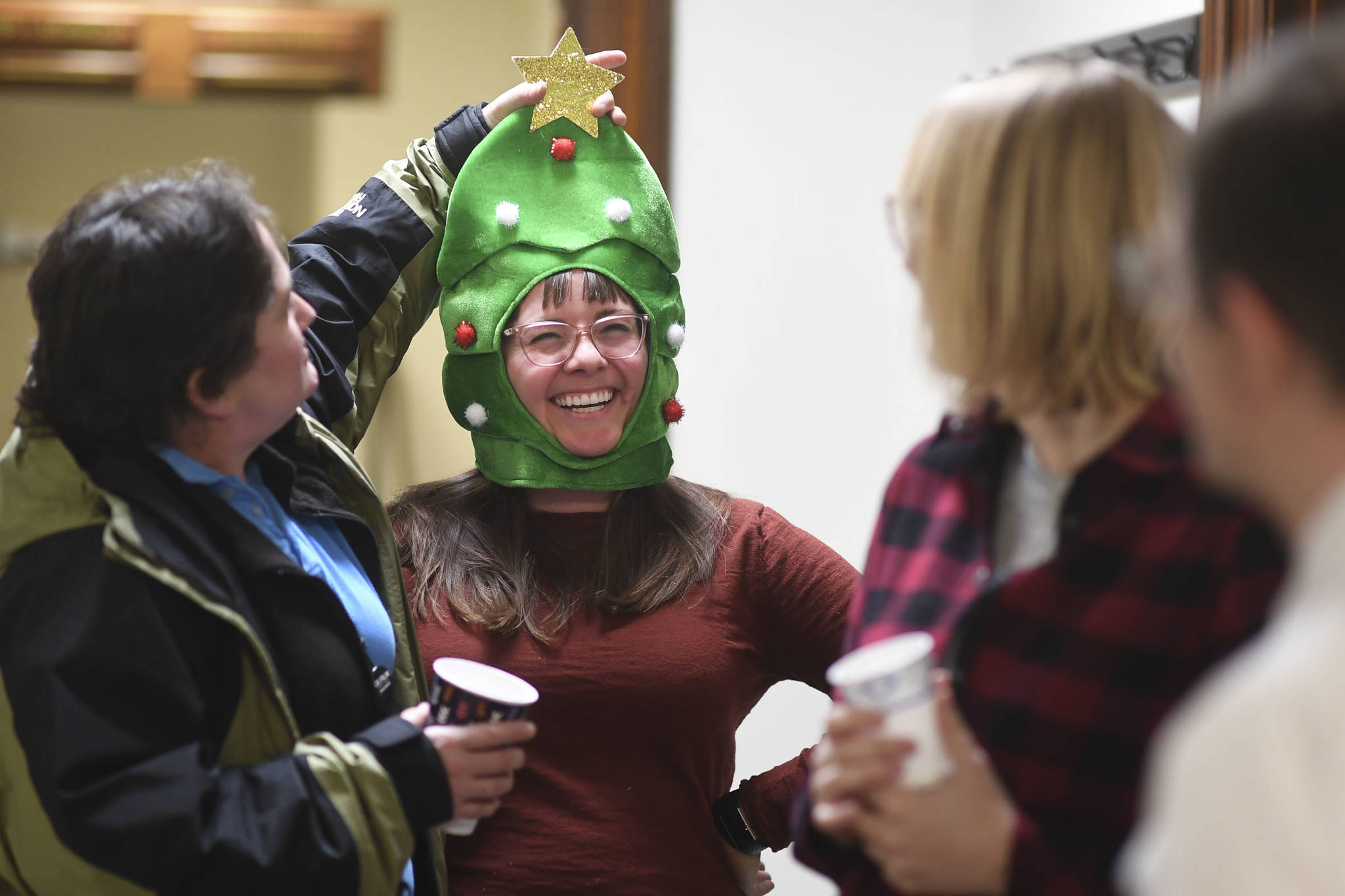 Caitlyn Ellis, a legislative aide for Rep. Andi Story, has her Christmas headgear adjusted by Rebecca Smith, left, during a legislative open house at the Capitol on Friday, Dec. 20, 2019. (Michael Penn | Juneau Empire)