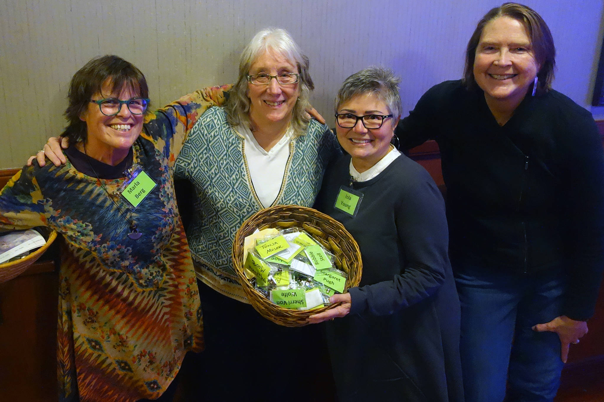 Marla Berg, organizing committee member for 100 Women Who Care Juneau; Kate Troll, who pitched the idea of donating to Renewable Juneau; Iola Young, organizing committee member for 100 Women Who Care Juneau; and Jane Lindsey, organizing committee member for 100 Women Who Care Juneau; smile with baskets filled with name tags and checks at the Hangar Ballroom, Thursday, Jan. 16, 2020. (Ben Hohenstatt | Juneau Empire)