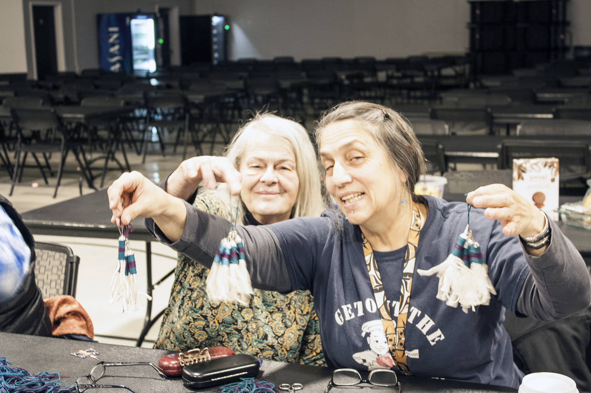 Kay Field Parker and Skeenyàa Tlàa Nancy Keen hold up bunches of zipper pulls, Sunday, Jan. 20, 2020. Both weavers were part of a 12-person group working to create the Chilkat tunic fringe zipper pulls that will be distributed to attendees of the Gathering of the Robes. (Ben Hohenstatt | Capital City Weekly)