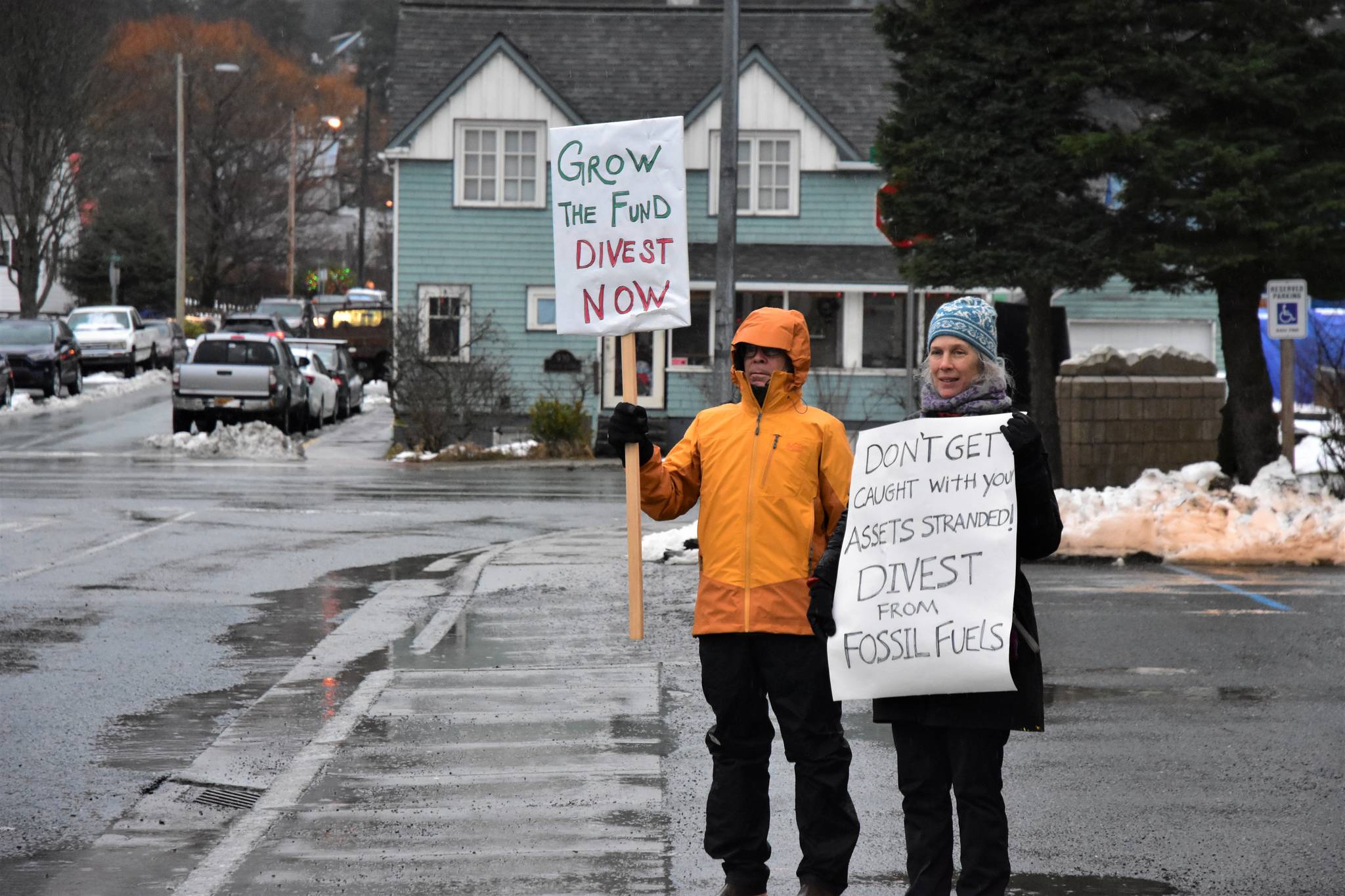 Dick Farnell, right, and Suzanne Cohen of environmental group 350Juneau hold signs outside the Alaska Permanent Fund Corporation building during APFC’s Board of Directors quarterly meeting on Wednesday. (Peter Segall | Juneau Empire)
