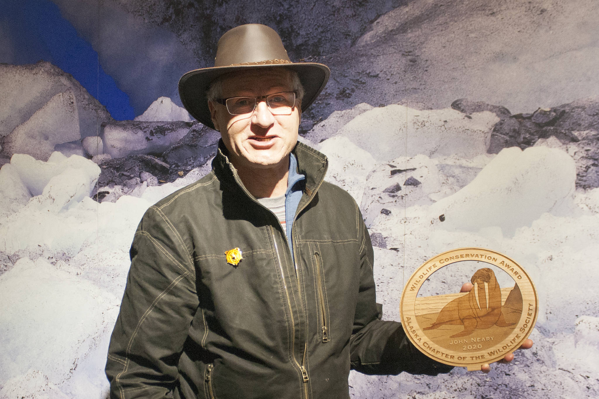 Former Mendenhall Glacier Visitor Center Director John Neary holds his 2020 Wildlife Conservation Lifetime Achievement Award from the Alaska Chapter of the Wildlife Society Friday evening at the visitor center. (Ben Hohenstatt | Juneau Empire)