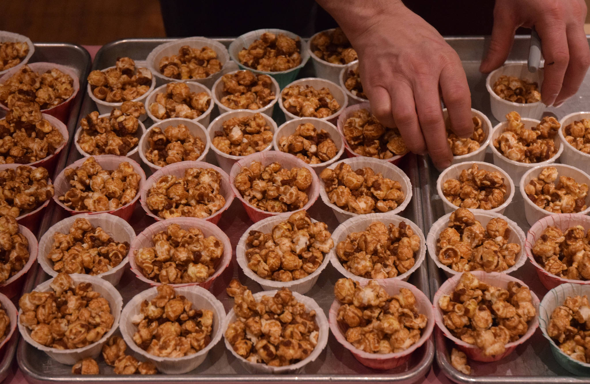 Phil Wheeler of Alaskan Fudge Co. arranges cups of bacon-flavored popcorn in February 2015 during the third annual Juneau Baconfest. (Michael Penn | Juneau Empire File)