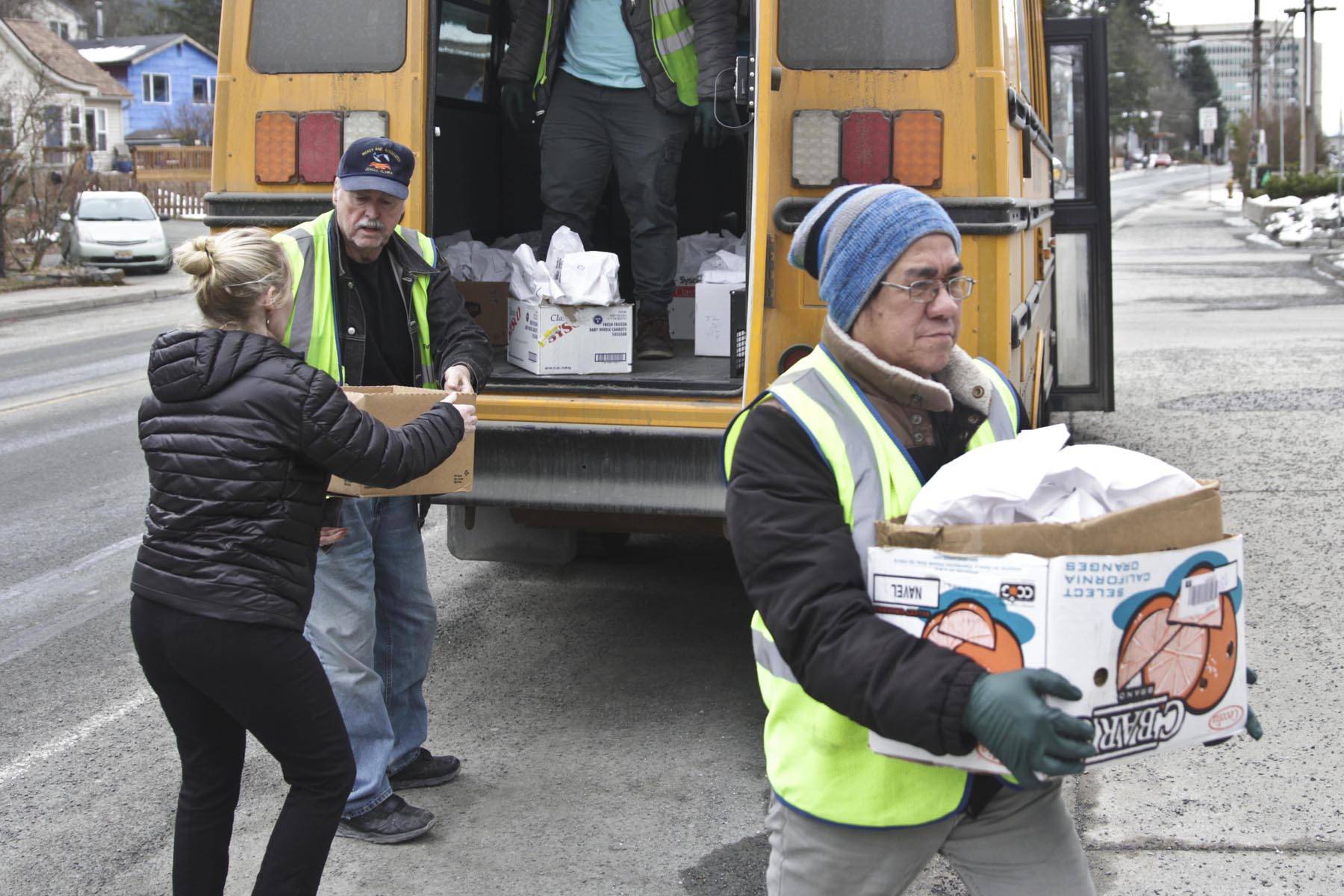 First Student employees and Juneau School District food services supervisor Adrianne Schwartz, left, carry student meals off the bus they’re being distributed from near Juneau-Douglas High School: Yadaa.at Kalé March 16, 2020. (Michael S. Lockett | Juneau Empire)