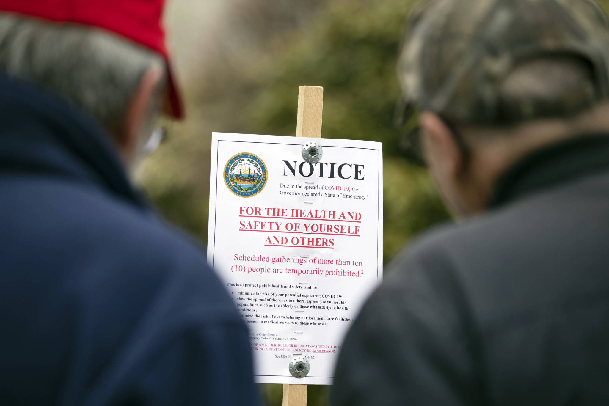 Tom Ploszaj, left, and Tony Stelik read a sign prohibiting gatherings of 10 or more people as they arrive at the State House for a scheduled protest against the state lockdown due to COVID-19, Saturday, April 18, 2020, in Concord, N.H. (AP Photo | Michael Dwyer)