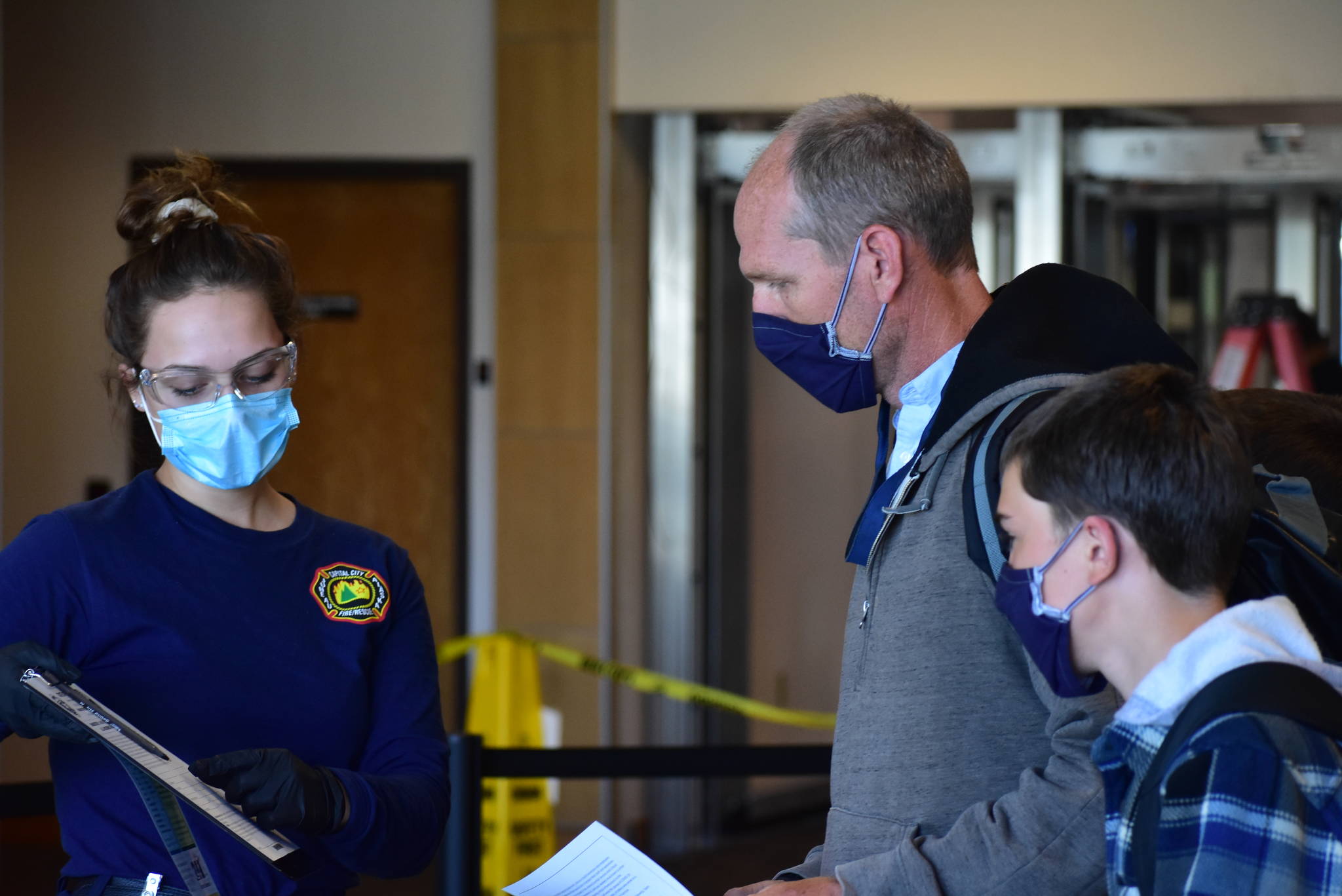 Peter Segall | Juneau Empire                                 A member of Capital City Fire/Rescue’s Airport Screening Task Force explains a questionnaire form to a family disembarking from a flight arriving at the Juneau International Airport on Wednesday, May 27, 2020.