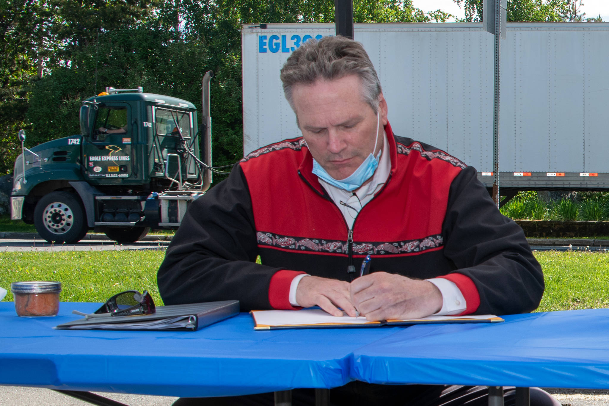 A mask hangs around Gov. Mike Dunleavy’s neck June 10 as he signs Gulkana Village agreement. Dunleavy on Tuesday encouraged Alaskans to wear face coverings. (Courtesy Photo | Office of Gov. Mike Dunleavy)