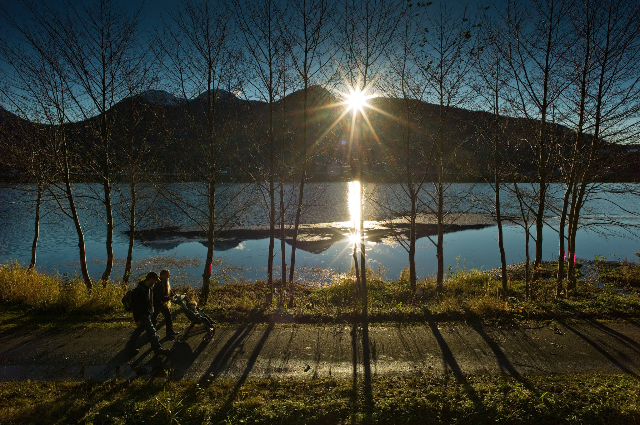 A family walks along Twin Lakes Tuesday afternoon as the sun sets behind Douglas Island. (Michael Penn / Juneau Empire File)