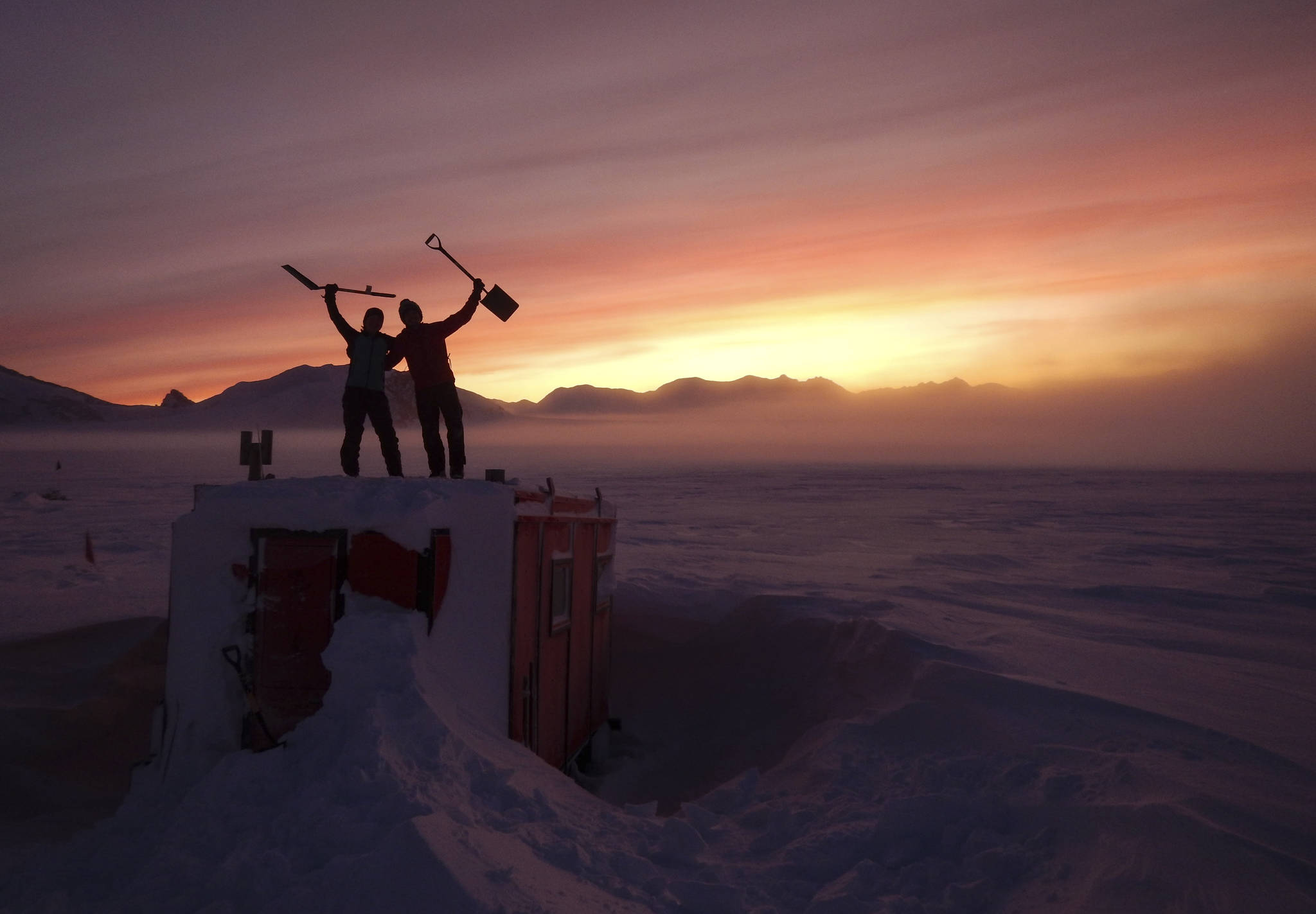 In this handout photo provided by British Antarctic Survey, field guides Sarah Crowsley, left, and Sam Hunt, right, pose for a photo after digging out the caboose, a container used for accommodation that can be moved by a tractor, at Adelaide island, in Antarctica on Friday, June 19, 2020. Antarctica remains the only continent without COVID-19 and now in Sept. 2020, as nearly 1,000 scientists and others who wintered over on the ice are seeing the sun for the first time in months, a global effort wants to make sure incoming colleagues don’t bring the virus with them. (Robert Taylor/British Antarctic Survey via AP)