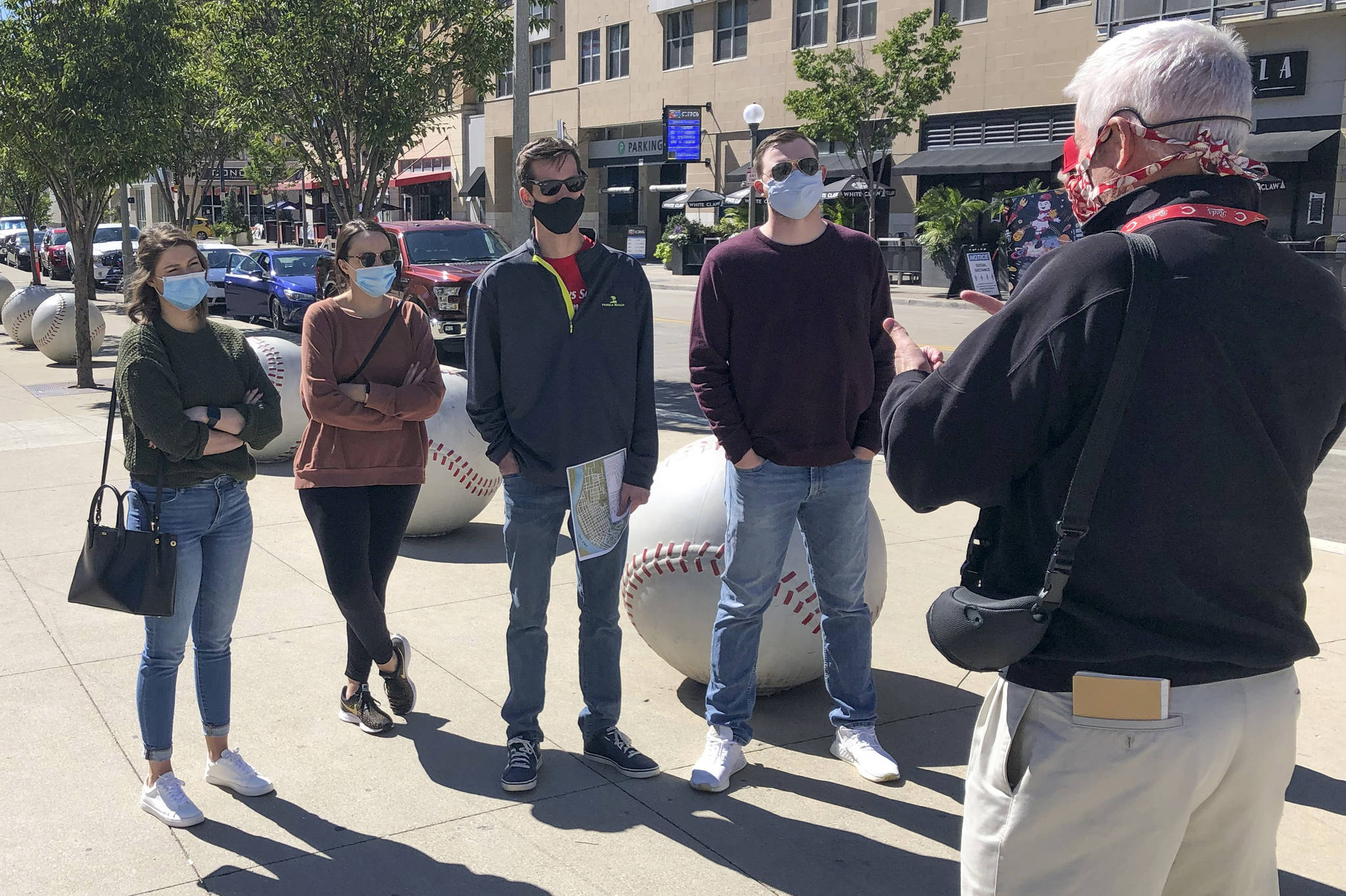 In this Sept. 20, 2020, photo, tour guide John Erardi, right, talks with a tour group on the sidewalk outside the Cincinnati Reds Great American Ball Park in Cincinnati. The walking tour was one of the few groups of people on the street as the Reds and White Sox were inside just an hour before the game without fans because of the pandemic. (AP Photo / Dan Sewell)