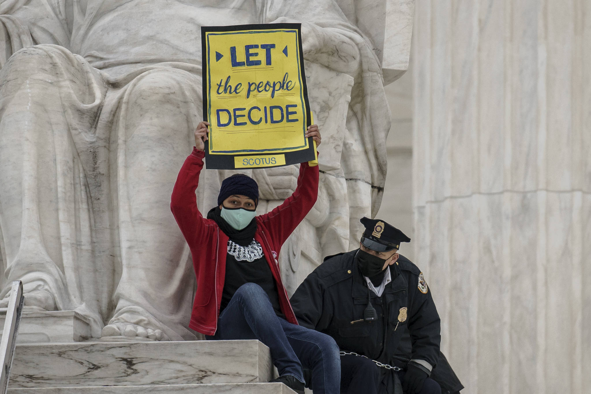 A protester opposed to the Senate's race to confirm Amy Coney Barrett is removed by police after chaining themselves to a railing and holding a sign while sitting atop the statue Contemplation of Justice, at the Supreme Court building in Washington, Sunday, Oct. 25, 2020. (AP Photo / J. Scott Applewhite)