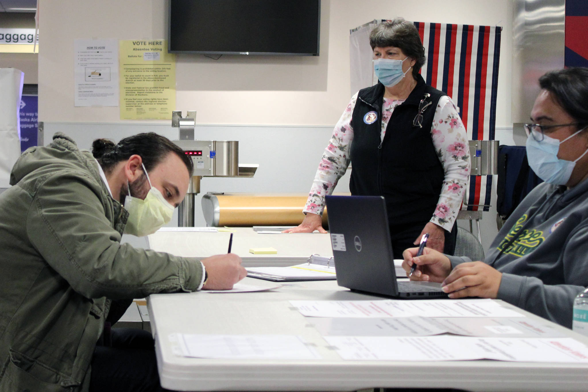 Ben Hohenstatt / Juneau Empire 
Nicolas Blanco, left, fills out paperwork ahead of voting absentee at Juneau International Airport on Election Day. Blanco recently moved to Juneau from North Carolina. He was assisted by election officials Carol Whelan, middle, and Lala Levale, right.