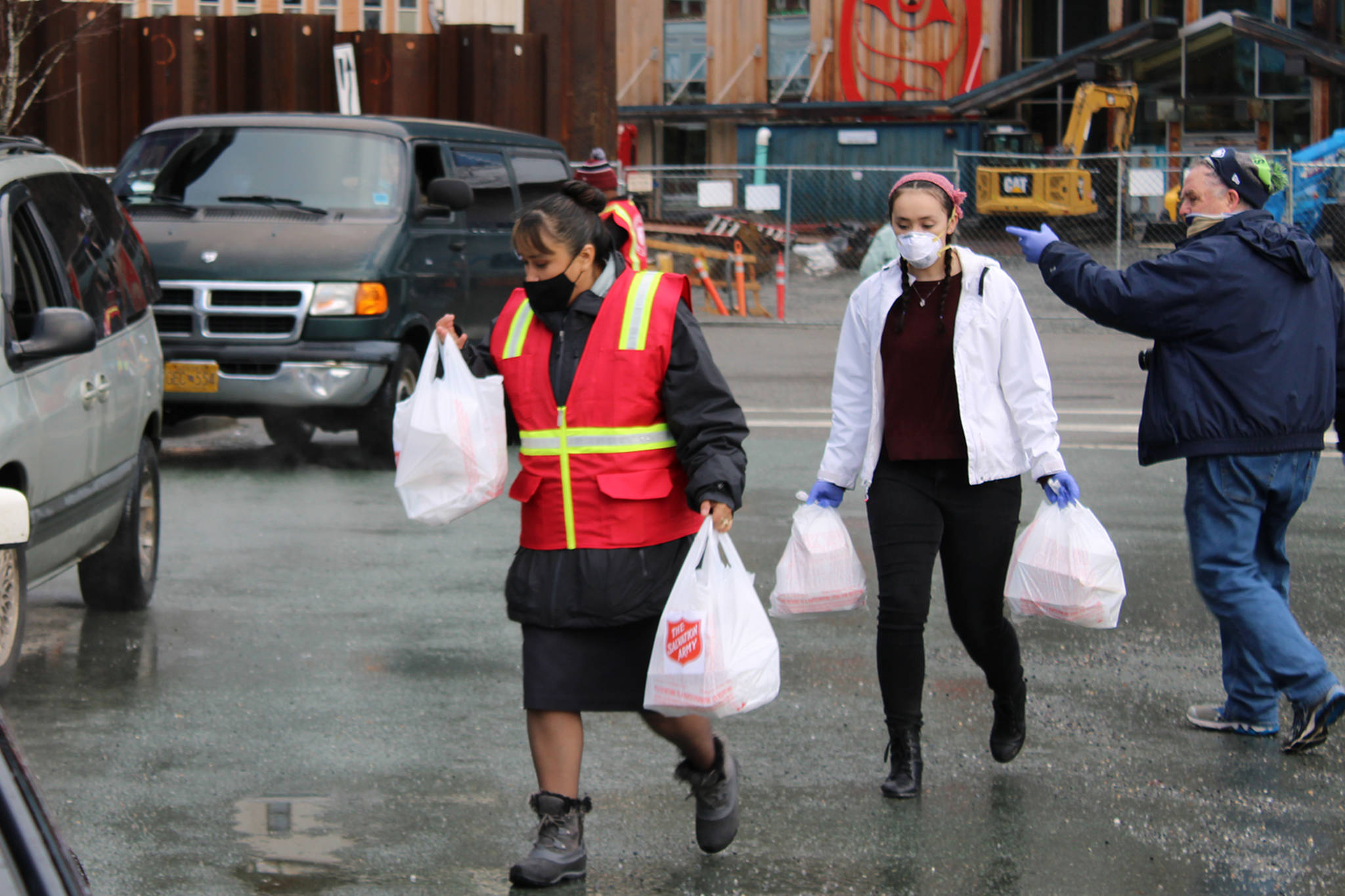 Salvation Army Officer Gina Halverson (left) and her daughter, Reilley Halverson (center), carry bags of meals to a waiting vehicle. Kirk Stagg (right) helps direct vehicles at the Downtown Transit Center on Thursday, Nov. 26. (Ben Hohenstatt / Juneau Empire)