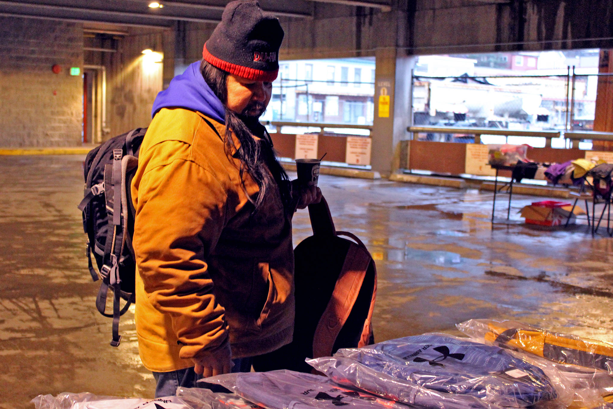 Charles Fawcett Jr. looks at backpacks provided by Central Council of Tlingit and Haida Indian Tribes of Alaska in the Marine Parking Garage on Saturday, Nov. 28. The parking garage was the site of Juneau Street Warming event meant to provide on-the-spot assistance to people experiencing homelessness. (Ben Hohenstatt / Juneau Empire)