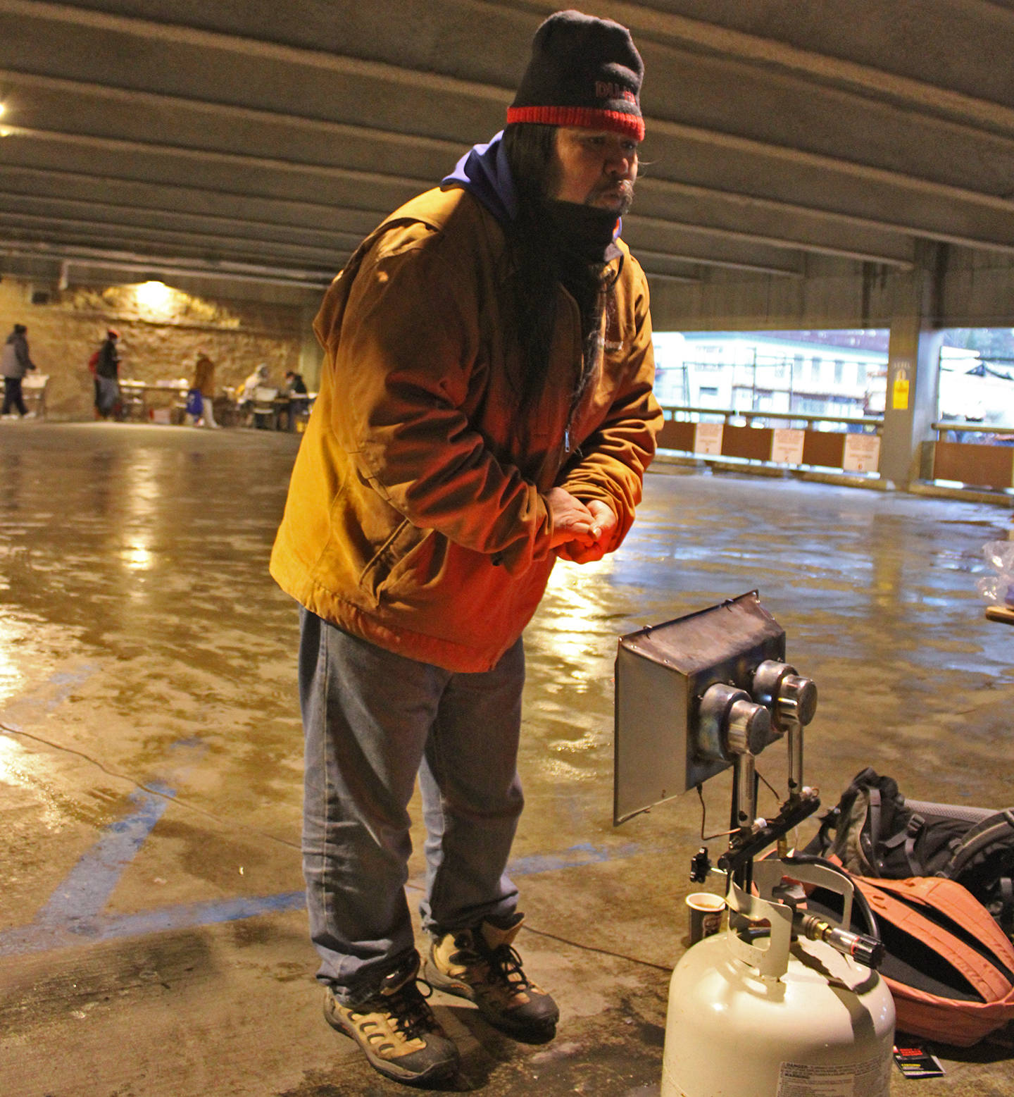Charles Fawcett Jr. warms up near a heater in the Marine Parking Garage on Saturday, Nov. 28. The parking garage was the site of Juneau Street Warming event meant to provide on-the-spot assistance to people experiencing homelessness. (Ben Hohenstatt / Juneau Empire)