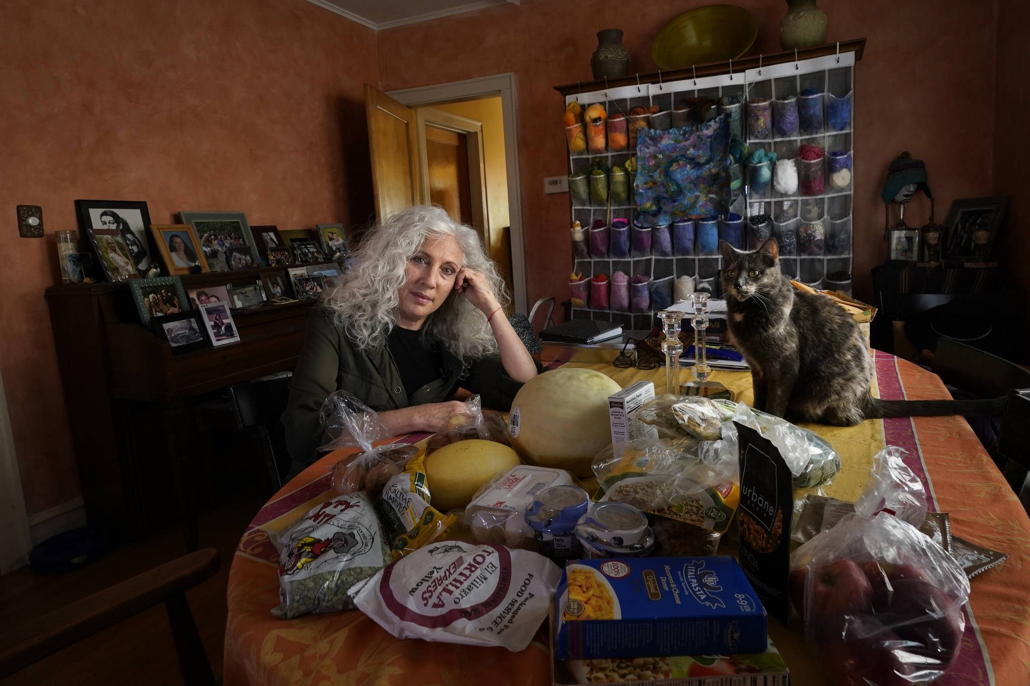 Phyllis Marder poses with her cat, Nellie, with food she recently obtained from a local food bank in the dining room of her home in Evanston, Ill., on Thursday, Nov. 5, 2020. At first, Marder, 66, didn’t tell anyone about going to food pantries. Then she had a change of heart. “Keeping a secret makes things get worse,” she says ’”… and makes me feel worse about myself, and so I decided that it was more important to talk about it.” (AP Photo/Charles Rex Arbogast)