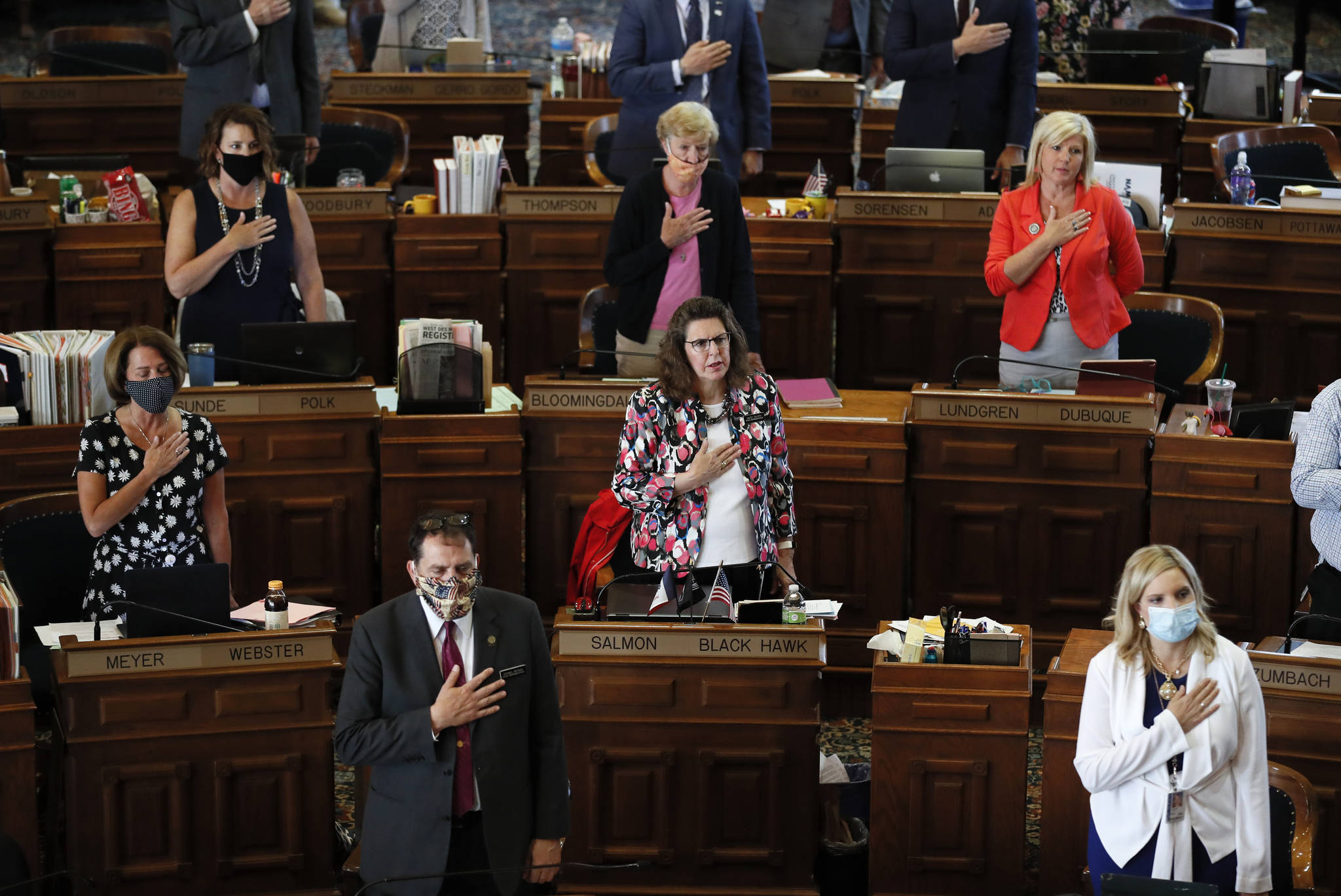 State Representatives stand at their desks during the Pledge of Allegiance in the Iowa House chambers, at the Statehouse in Des Moines, Iowa, in June 2020. As states brace for a coronavirus surge following holiday gatherings, one place stands out as a potential super-spreader site, the statehouses where lawmakers will help shape the response to the pandemic. (AP Photo / Charlie Neibergall)