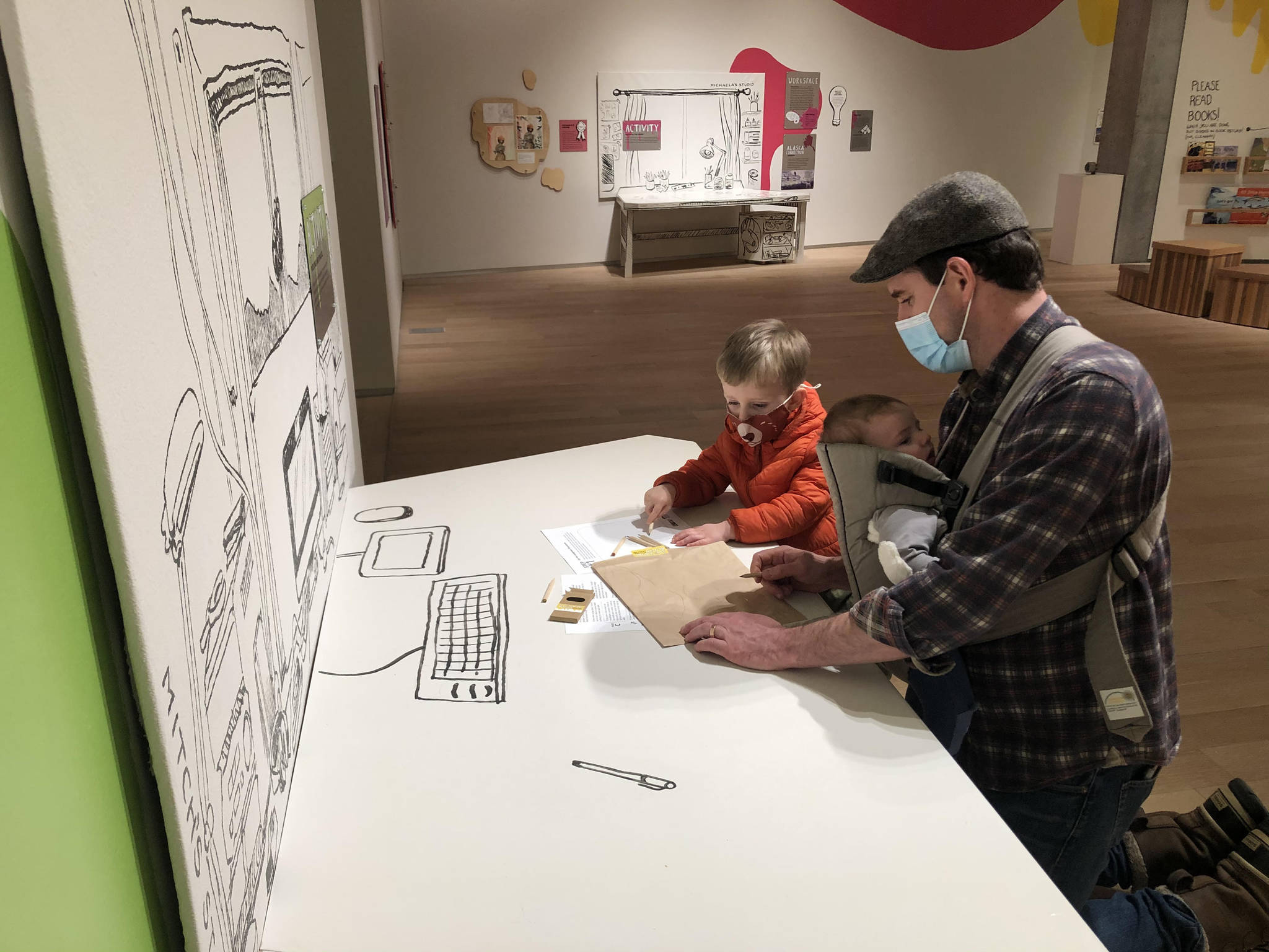 Sebastian Taylor-Manning pauses to sketch at a replica of an Alaskan illustrator’s desk. His brother McClain Taylor-Manning and his father, Chris Taylor, look on during a recent visit to the State Museum to see the new exhibit, "Illustrating Alaska: Artists Making Children’s Books", on display through April 3. (Courtesy Photo/Jackie Manning)