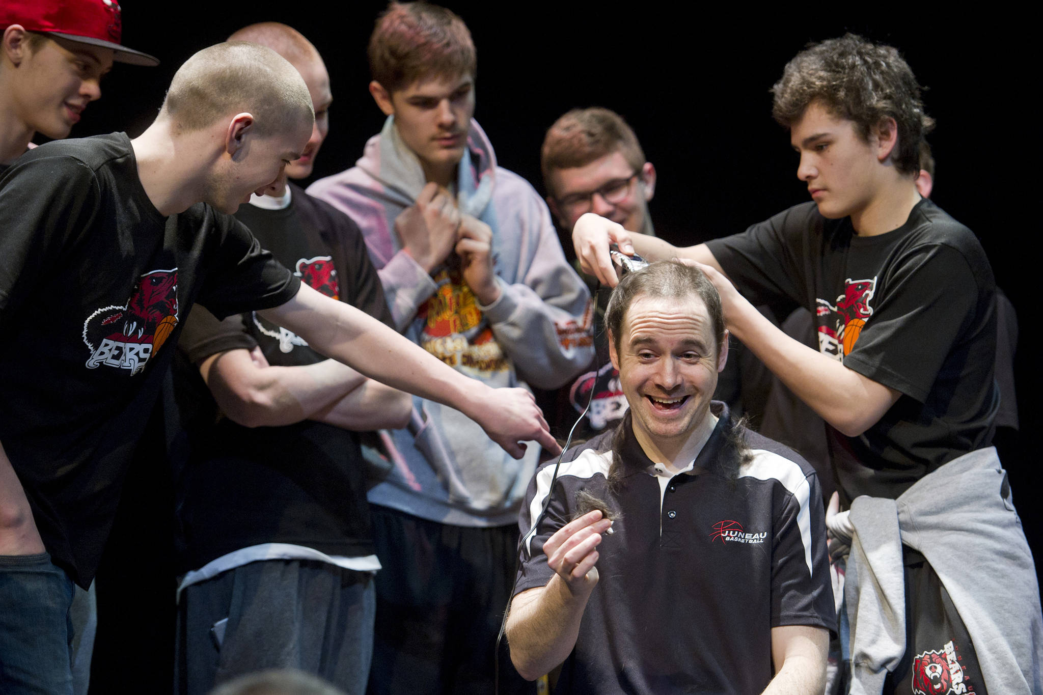 Juneau-Douglas High School head basketball coach Robert Casperson gets his hair cut on stage by senior Treyson Ramos during a school assembly Wednesday, holding up his end of the bargain that he would shave his head if his team won the state championship title. Casperson said he trusted the 2016 team's senior class a lot.