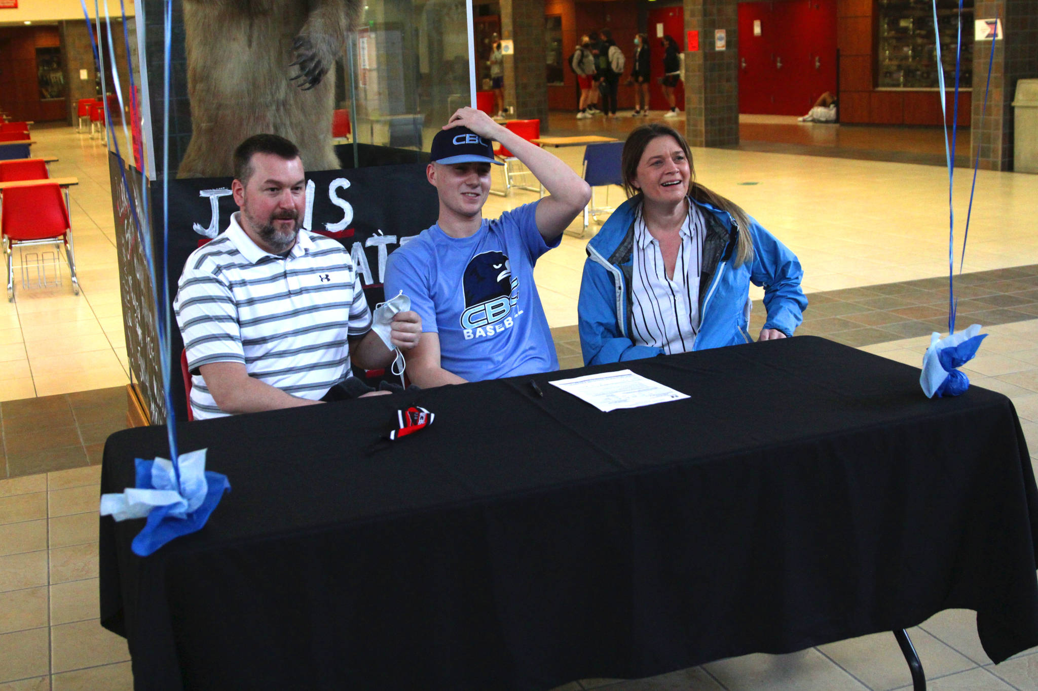 Juneau-Douglas High School Yadaa.at Kalé senior Garrett Bryant, sitting with parents Ronnie Bryant and Blair Ramsdell, signed his letter of intent to play baseball for Columbia Basin College at JDHS on March 11, 2021. (Michael S. Lockett / Juneau Empire)