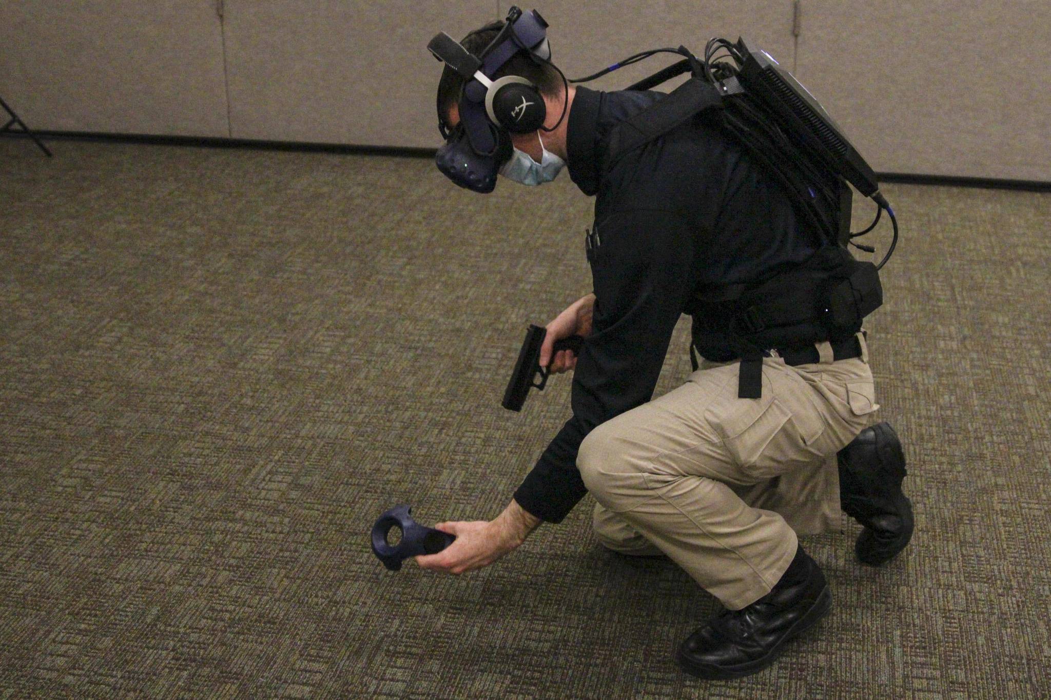 Detective Patrick Taylor picks up controllers representing his sidearm and police utility items during VR training simulation on March 17, 2021. The computer maintaining the simulation is visible on his back. (Michael S. Lockett / Juneau Empire)
