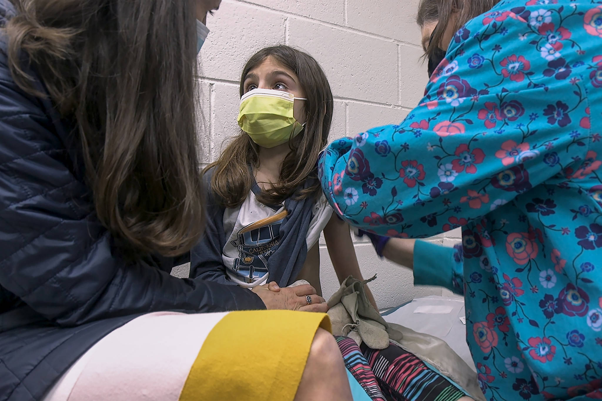 In this Wednesday, March 24, 2021 image from video provided by Duke Health, Alejandra Gerardo, 9, looks up to her mom, Dr. Susanna Naggie, as she gets the first of two Pfizer COVID-19 vaccinations during a clinical trial for children at Duke Health in Durham, N.C. In the U.S. and abroad, researchers are beginning to test younger and younger kids, to make sure the shots are safe and work for each age. (Shawn Rocco / Duke Health)