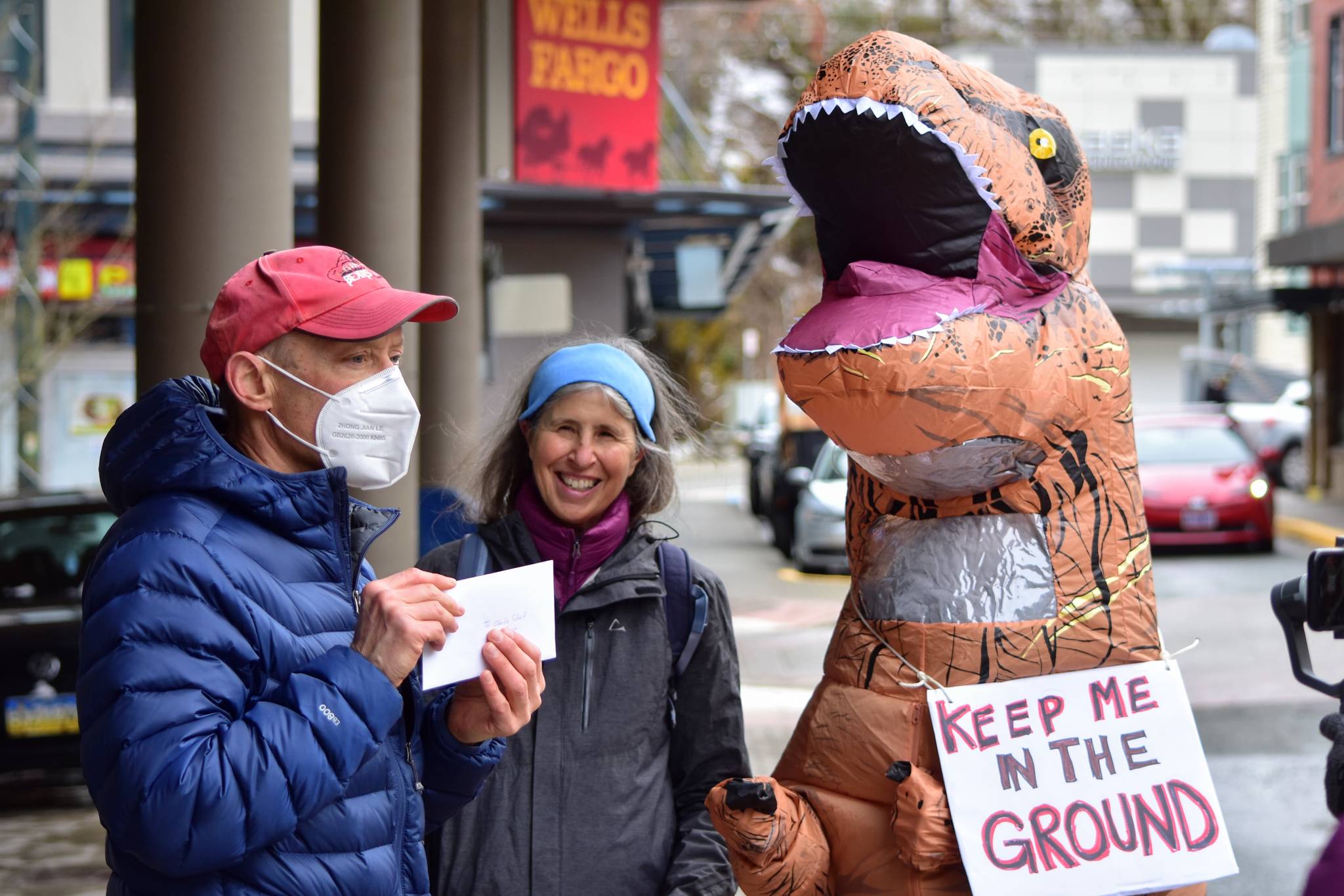Doug Woodby, co-chair of environmental group 350Juneau, holds up a letter addressed to the CEO of Wells Fargo alongside Irene Alexakos and Dick Farnell, wearing the costume. The group delivered the letter urging divestment from the fossil fuel industry to the bank's branch in downtown Juneau on Friday, April 2, 2021. (Peter Segall / Juneau Empire)
