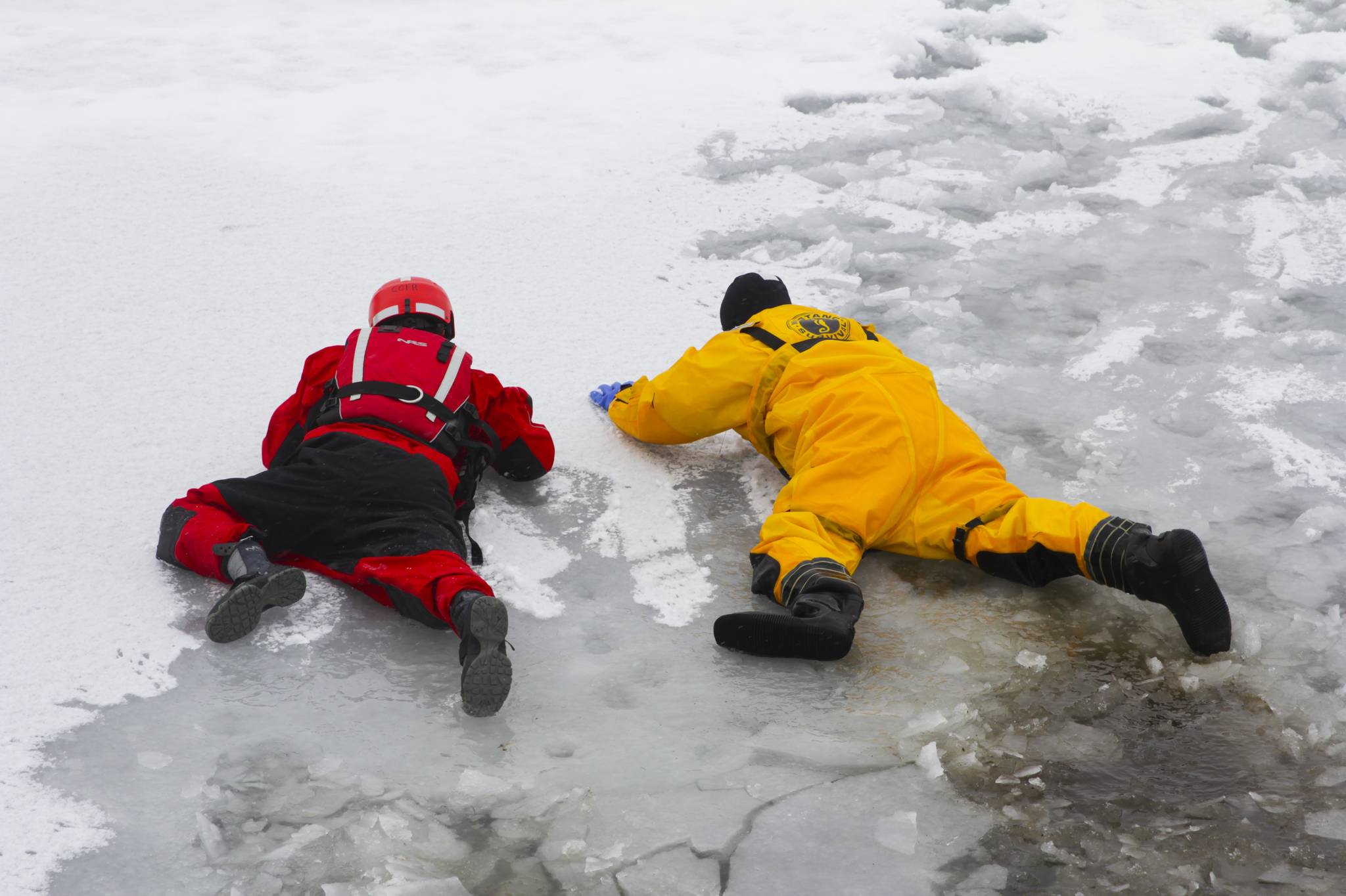 Capt. Jayme Johns, in yellow, head of the Capital City Fire/Rescue’s water rescue team, shows firefighter Liam Van Sickle, left, how to safely cross treacherous ice during CCFR’s annual ice rescue training at Twin Lakes on April 7, 2021. (Michael S. Lockett / Juneau Empire)