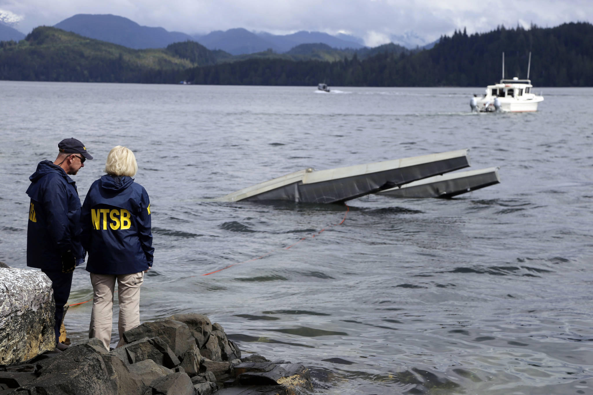 In this photo provided by the National Transportation Safety Board, NTSB investigator Clint Crookshanks, left, and member Jennifer Homendy stand near the site of some of the wreckage of the DHC-2 Beaver, Wednesday, May 15, 2019, that was involved in a midair collision near Ketchikan, Alaska, a couple of days earlier. The pilots of two Alaskan sightseeing planes that collided in midair couldn’t see the other aircraft because airplane structures or a passenger blocked their views, and they didn’t get electronic alerts about close aircraft because safety systems weren’t working properly. That’s what the staff of the National Transportation Safety board found in their investigation. (Peter Knudson / NTSB)